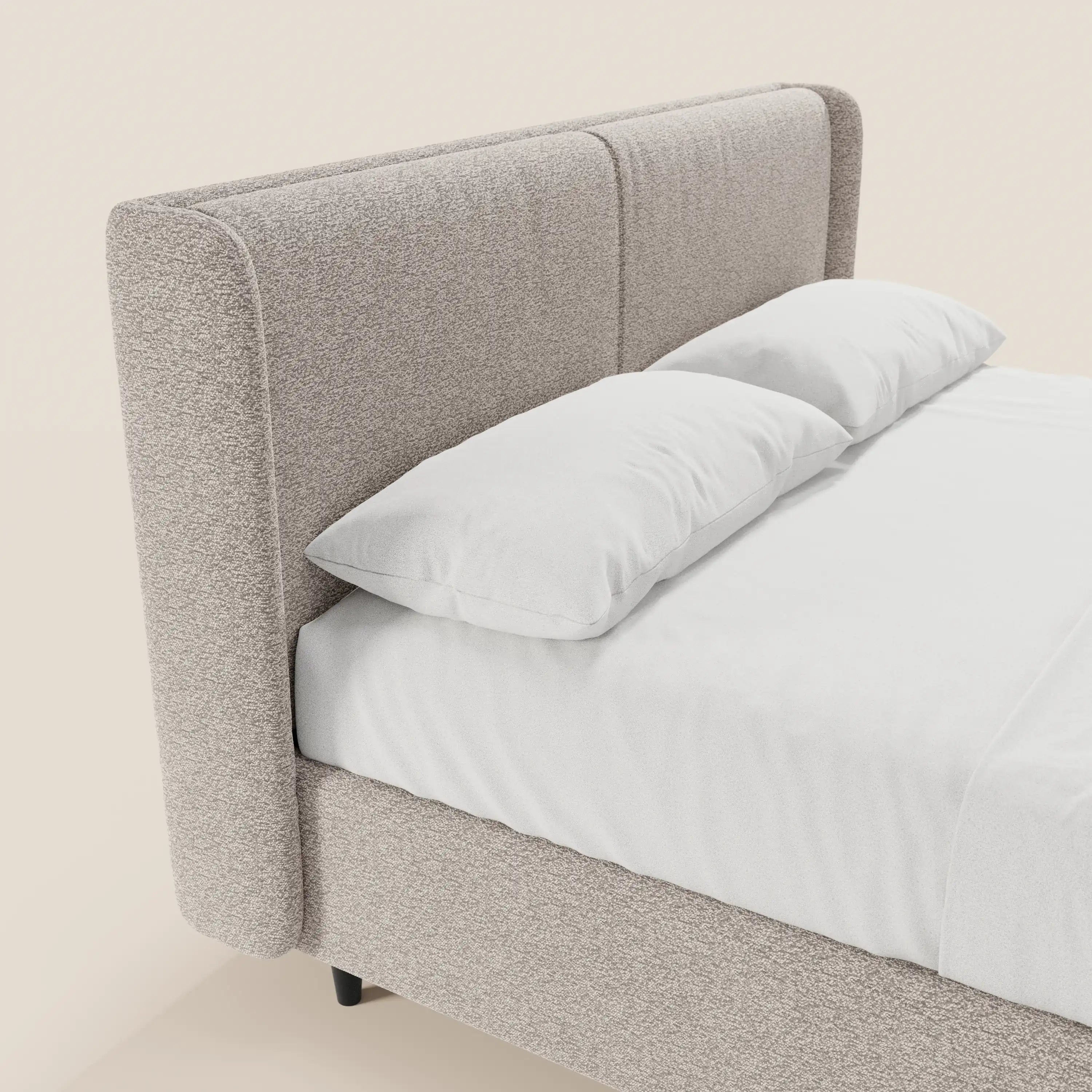 Un primo piano del letto di design VALKIRIA di Letti.store ne mette in risalto il tessuto Oeko-Tex®, la testiera avvolgente, i 2 cuscini imbottiti, il vano contenitore e le gambe corte di colore scuro, il tutto su uno sfondo chiaro con cuscini bianchi e lenzuolo con angoli.