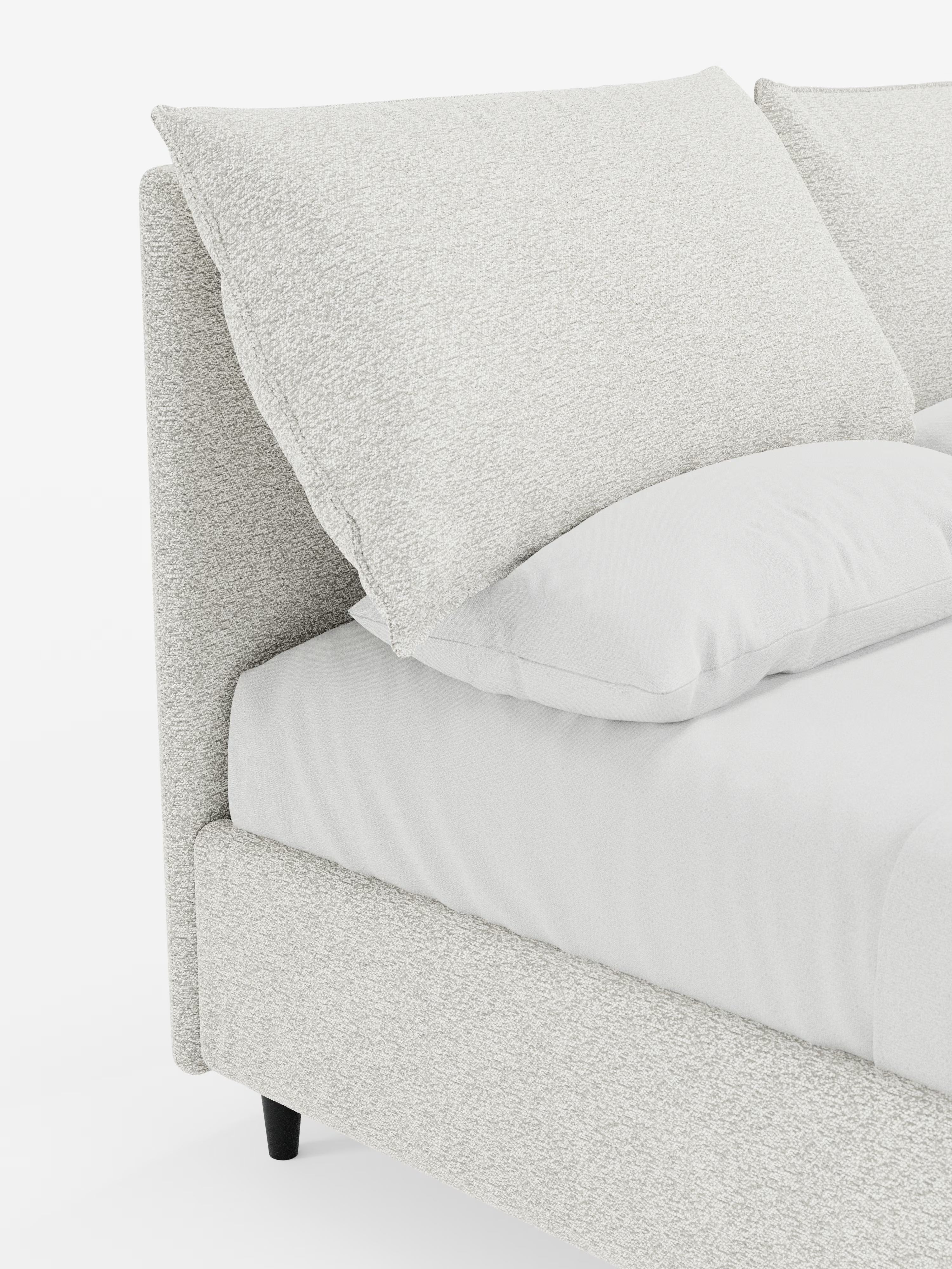 Primo piano del letto imbottito ZAYRON con contenitore e morbidi cuscini regolabili di Letti.store, che mette in risalto il suo design moderno con testiera e struttura in tessuto grigio chiaro testurizzato certificato Oeko-Tex®. Il letto è dotato di due grandi cuscini regolabili, un materasso e un cuscino più piccolo abbinato — tutti rivestiti con un tessuto chiaro simile — e poggia su corte gambe nere su uno sfondo bianco.