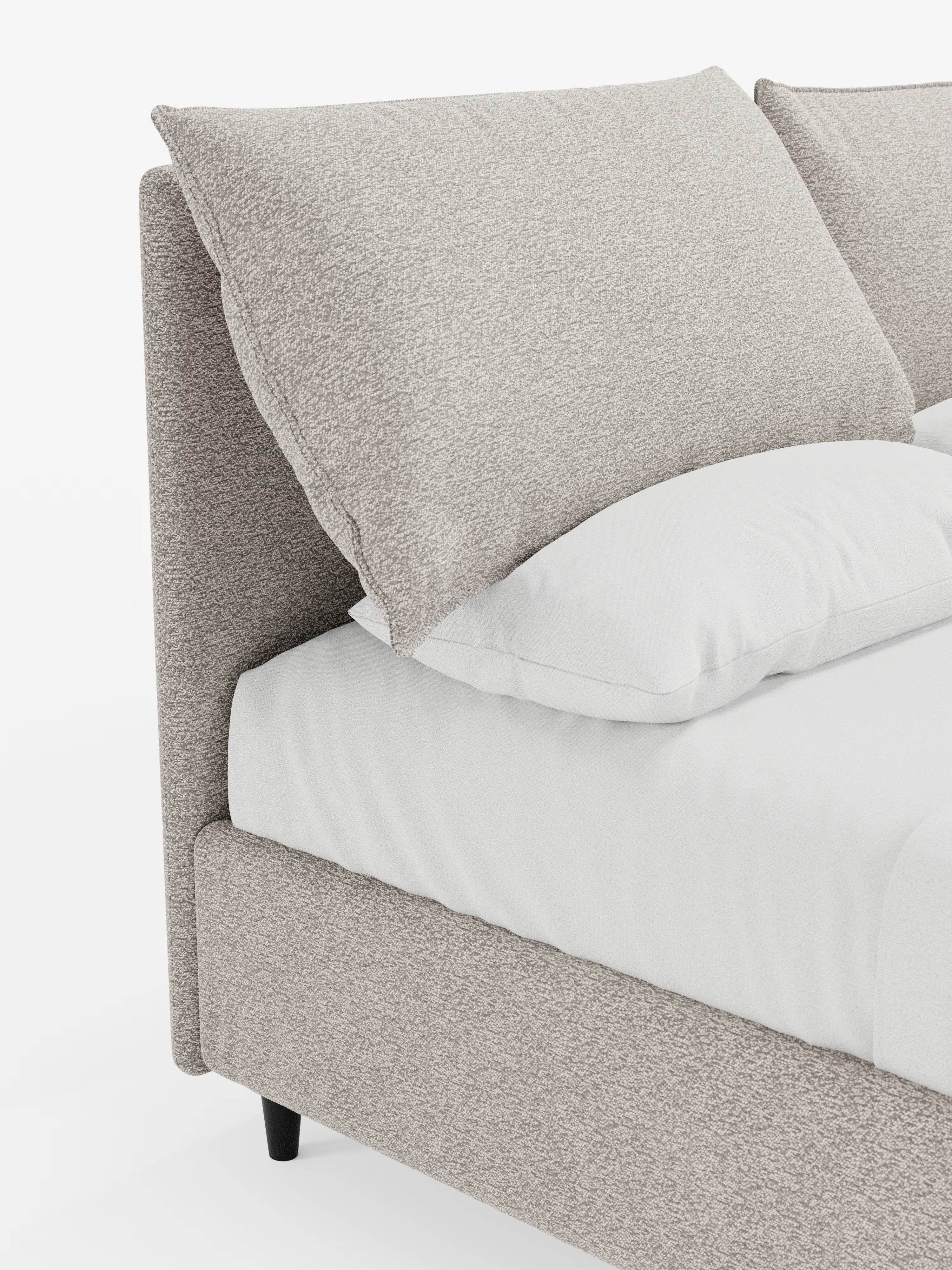 Primo piano del letto imbottito con contenitore ZAYRON di Letti.store, caratterizzato da una struttura imbottita moderna, certificata Oeko-Tex®, in tessuto beige testurizzato. L'immagine mette in risalto l'ampia testiera angolare regolabile e i morbidi cuscini regolabili, abbinati a un materasso bianco e a un morbido cuscino bianco. La scena è illuminata da una luce intensa su uno sfondo pulito e minimalista.