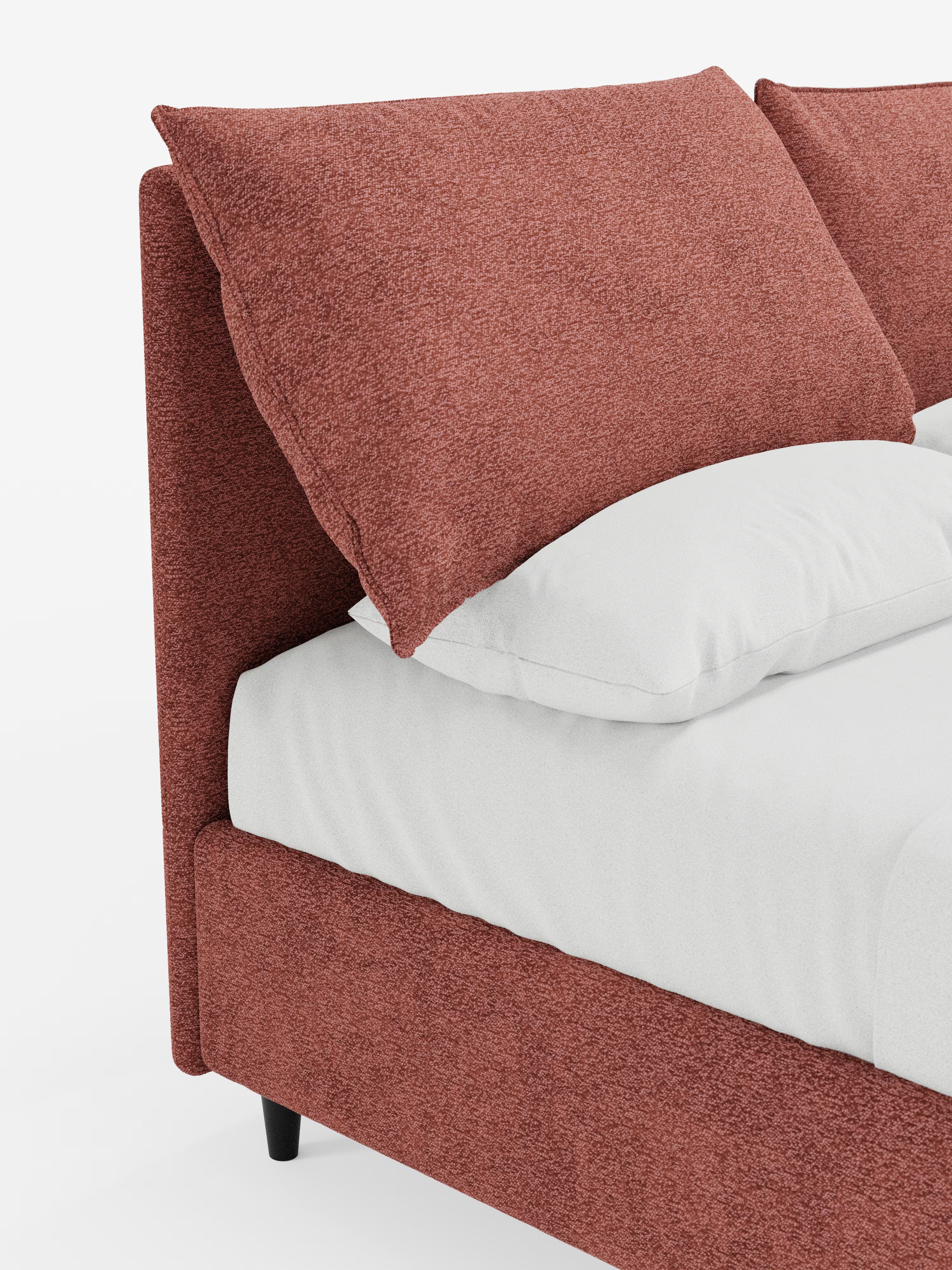 Primo piano del letto imbottito con contenitore ZAYRON di Letti.store, che mette in risalto la struttura e la testiera in tessuto color bruno-rossastro certificato Oeko-Tex®, insieme ai grandi cuscini coordinati e regolabili. Il letto moderno è rifatto con cura con lenzuola e federe bianche, su uno sfondo bianco a tinta unita che ne esalta il colore e la trama.