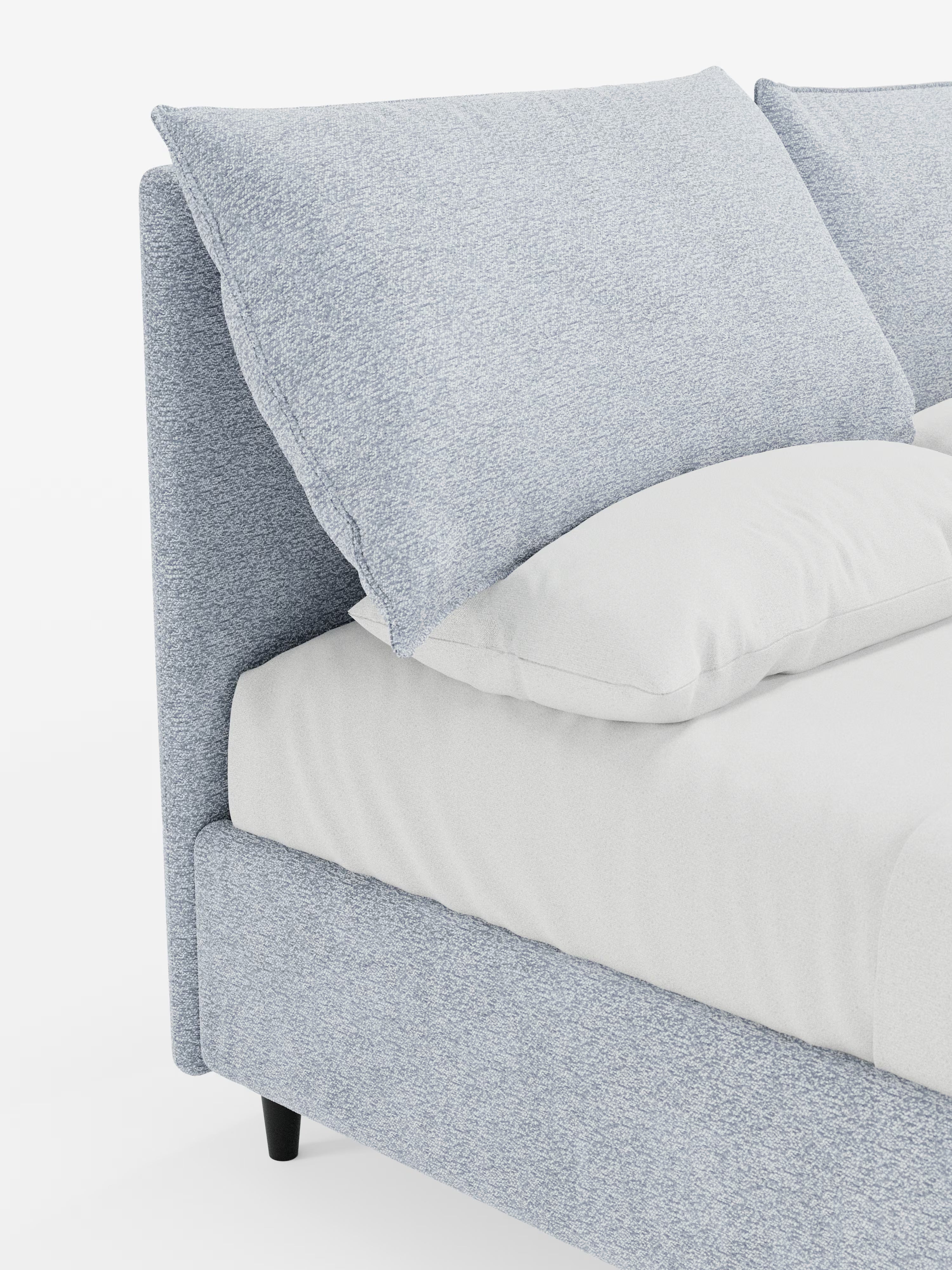 Una vista laterale ravvicinata del letto imbottito ZAYRON con contenitore e morbidi cuscini regolabili di Letti.store, un moderno letto imbottito in tessuto azzurro certificato Oeko-Tex®, caratterizzato da grandi cuscini imbottiti regolabili sulla testiera e da un lenzuolo bianco sporco, presentato su uno sfondo bianco.