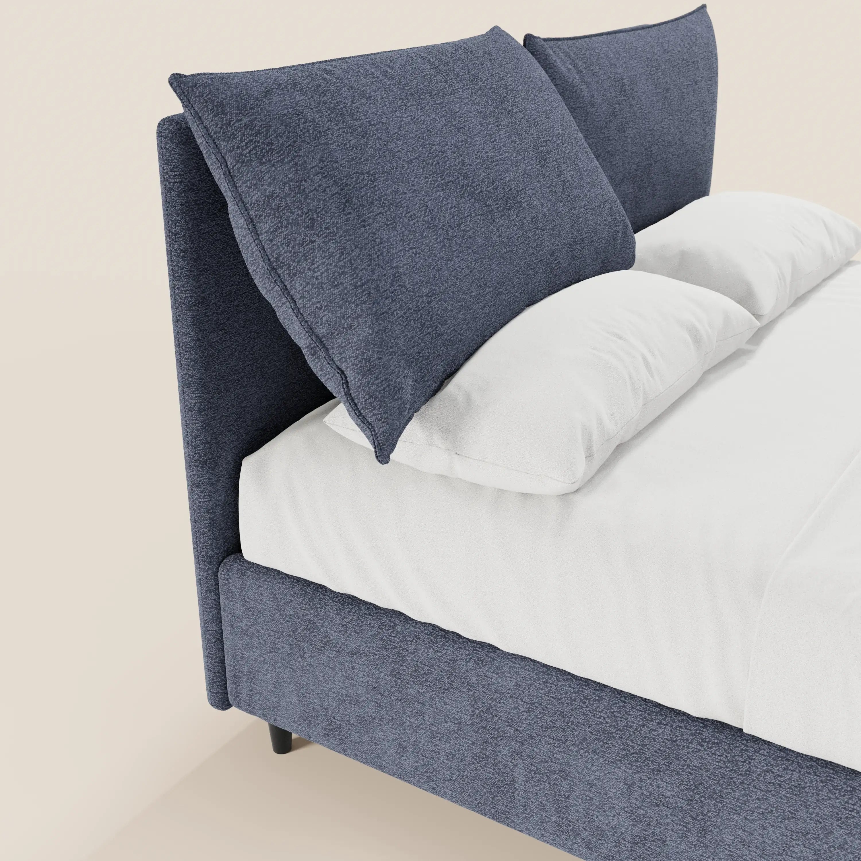 Il letto imbottito ZAYRON di Letti.store è dotato di vano contenitore, morbidi cuscini regolabili e un design moderno in tessuto blu certificato Oeko-Tex®, con grandi cuscini blu e lenzuola bianche su uno sfondo chiaro.