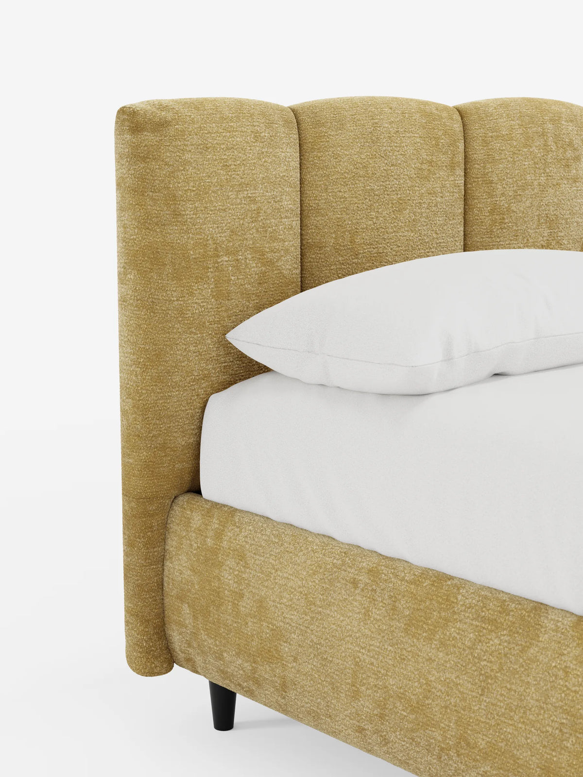 Un letto ARKAM color giallo senape, imbottito, con contenitore e testiera a trapuntatura verticale, rivestito con un lenzuolo bianco e un cuscino su uno sfondo a tinta unita, con una piccola gamba nera visibile.