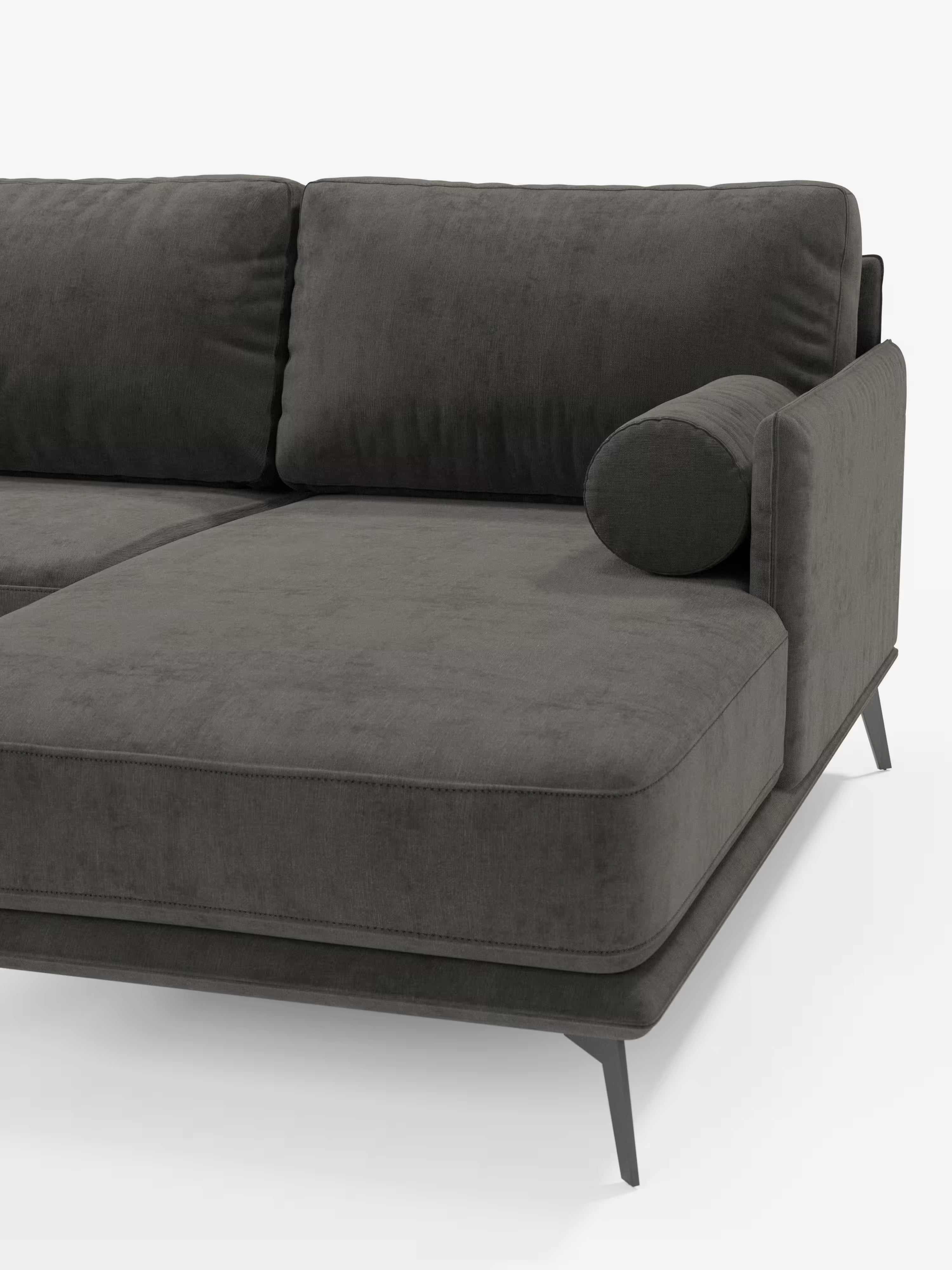 Il divano moderno angolare con penisola Basalto di Divani.Store è rivestito in tessuto T31 smacchiabile, di colore grigio antracite, morbido e vellutato, con soffici cuscini imbottiti in piuma, un cuscino cilindrico integrato nel bracciolo e una robusta base in metallo con eleganti gambe angolate. Questo divano componibile Made in Italy incarna un'eleganza raffinata ed è parzialmente visibile su uno sfondo bianco a tinta unita.