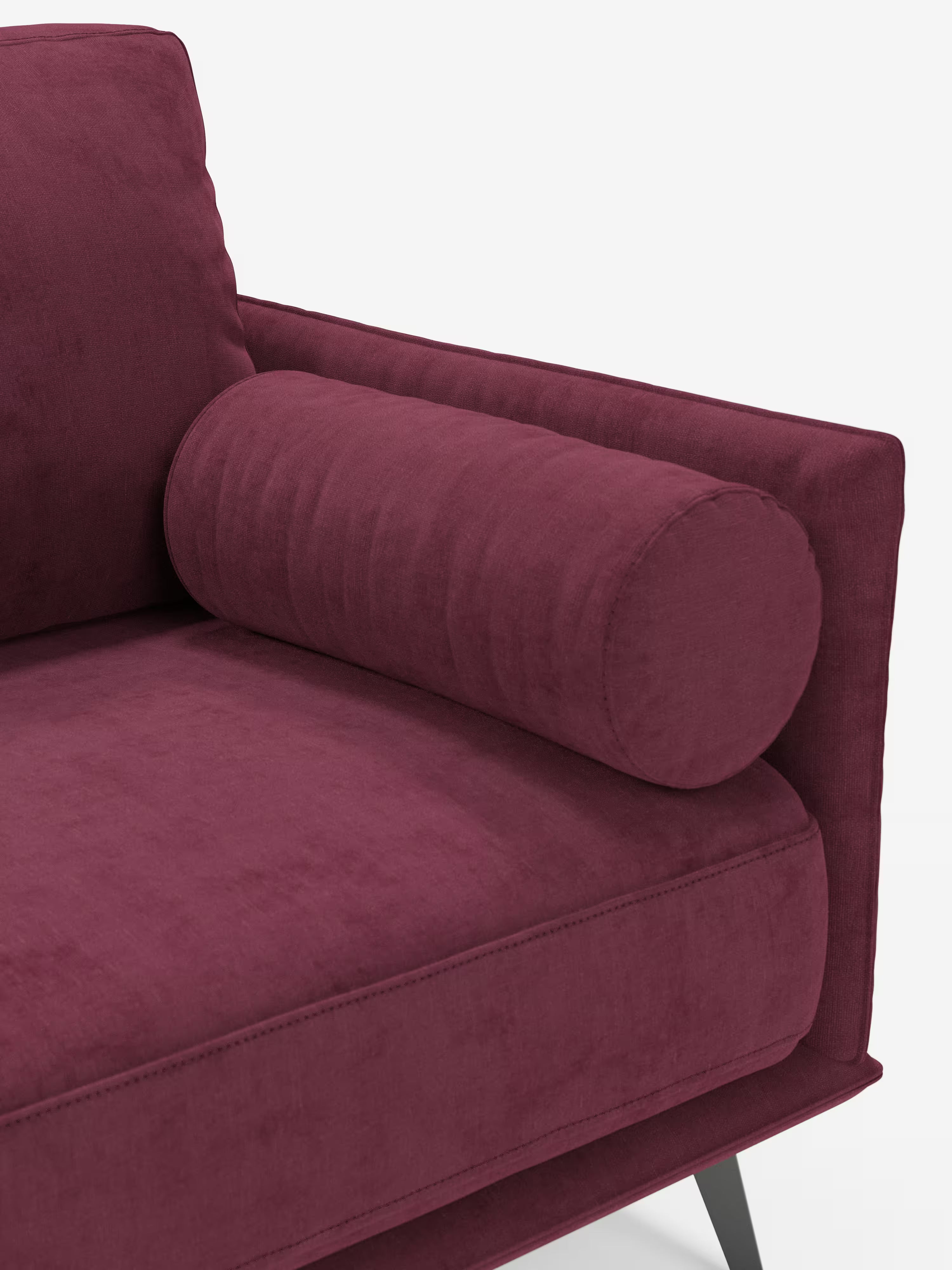 Un primo piano del divano lineare a 2 posti "Basalto" di Divani.Store, rivestito in tessuto smacchiabile T31 color bordeaux intenso. L'immagine mostra una seduta rettangolare, un cuscino cilindrico e una parte dello schienale e del bracciolo, tutti rivestiti con lo stesso tessuto. Questo divano dal design minimalista poggia su gambe angolate in metallo nero.