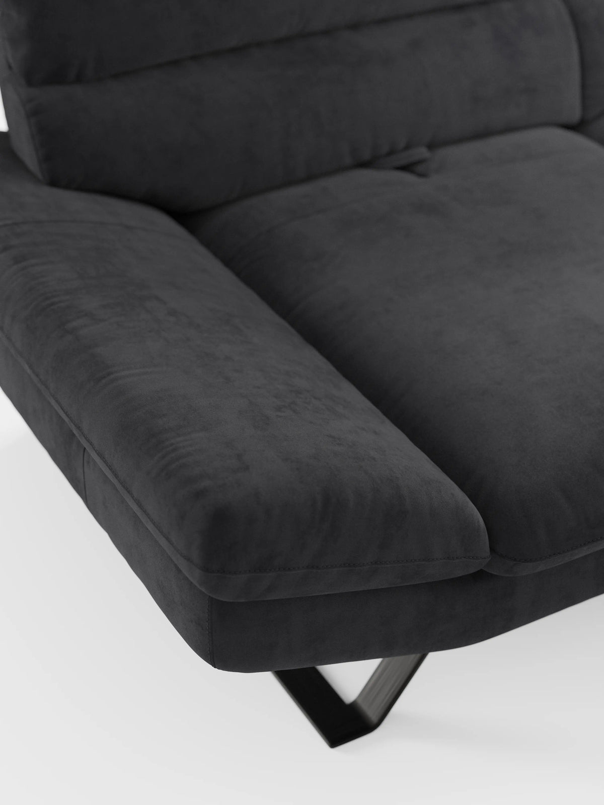 Primo piano del divano Eclipse, un modello moderno a 2 e 3 posti con schienali scorrevoli di Divani.Store, rivestito in elegante microfibra T11 resistente alle macchie. Questo divano contemporaneo color grigio scuro presenta braccioli ampi e imbottiti, cuscini morbidi e piedini alti ed eleganti in metallo nero. La trama del rivestimento è chiaramente visibile, sottolineando una sensazione di morbidezza e comfort modulabile. In primo piano su uno sfondo bianco a tinta unita.