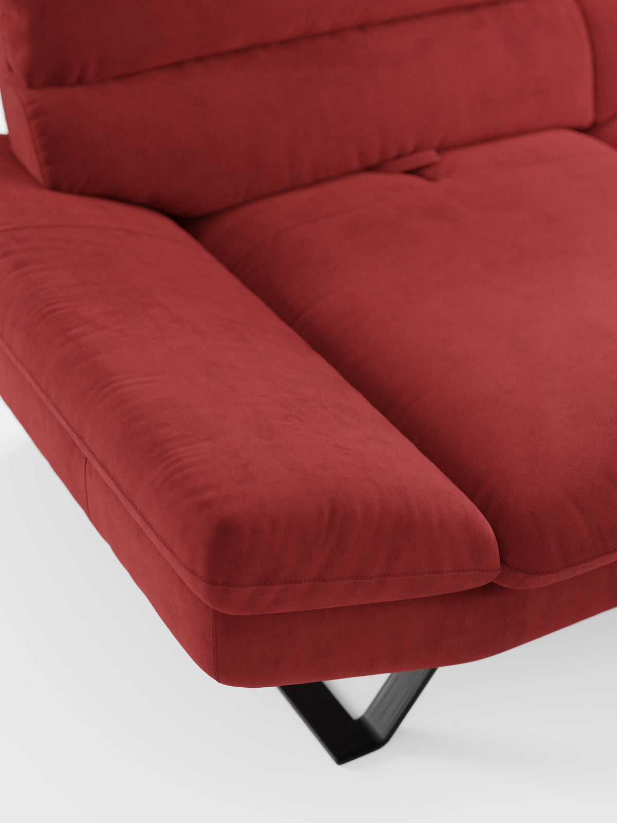 Primo piano del divano Eclipse dal design moderno a 2 e 3 posti di Divani.Store in un rosso vivace, rivestito in elegante microfibra smacchiabile T11 resistente alle macchie. Il divano è caratterizzato da ampi braccioli imbottiti e da schienali traslanti per un comfort personalizzabile e modulabile. La sua gamba angolare in metallo nero poggia su un pavimento bianco, mentre l’immagine si concentra sul dettaglio dell’angolo per mettere in risalto la texture morbida e l’estetica contemporanea.
