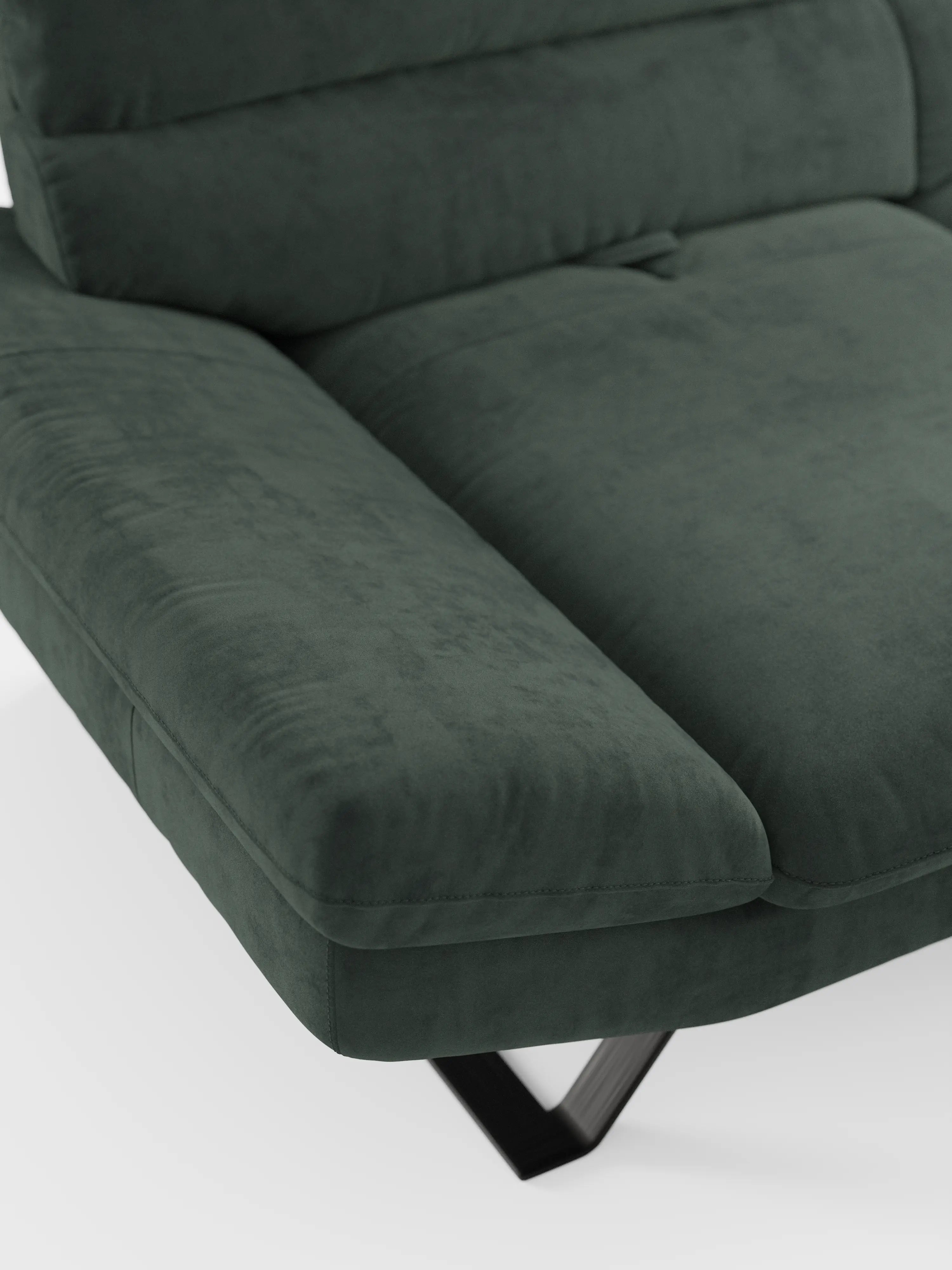 Un primo piano del divano Eclipse dal design moderno di Divani.Store, rivestito in elegante microfibra T11 verde scuro, mette in risalto il bracciolo sinistro, il cuscino della seduta e i piedini metallici alti e angolati su un pavimento bianco. Il tessuto smacchiabile appare morbido, soffice e invitante.