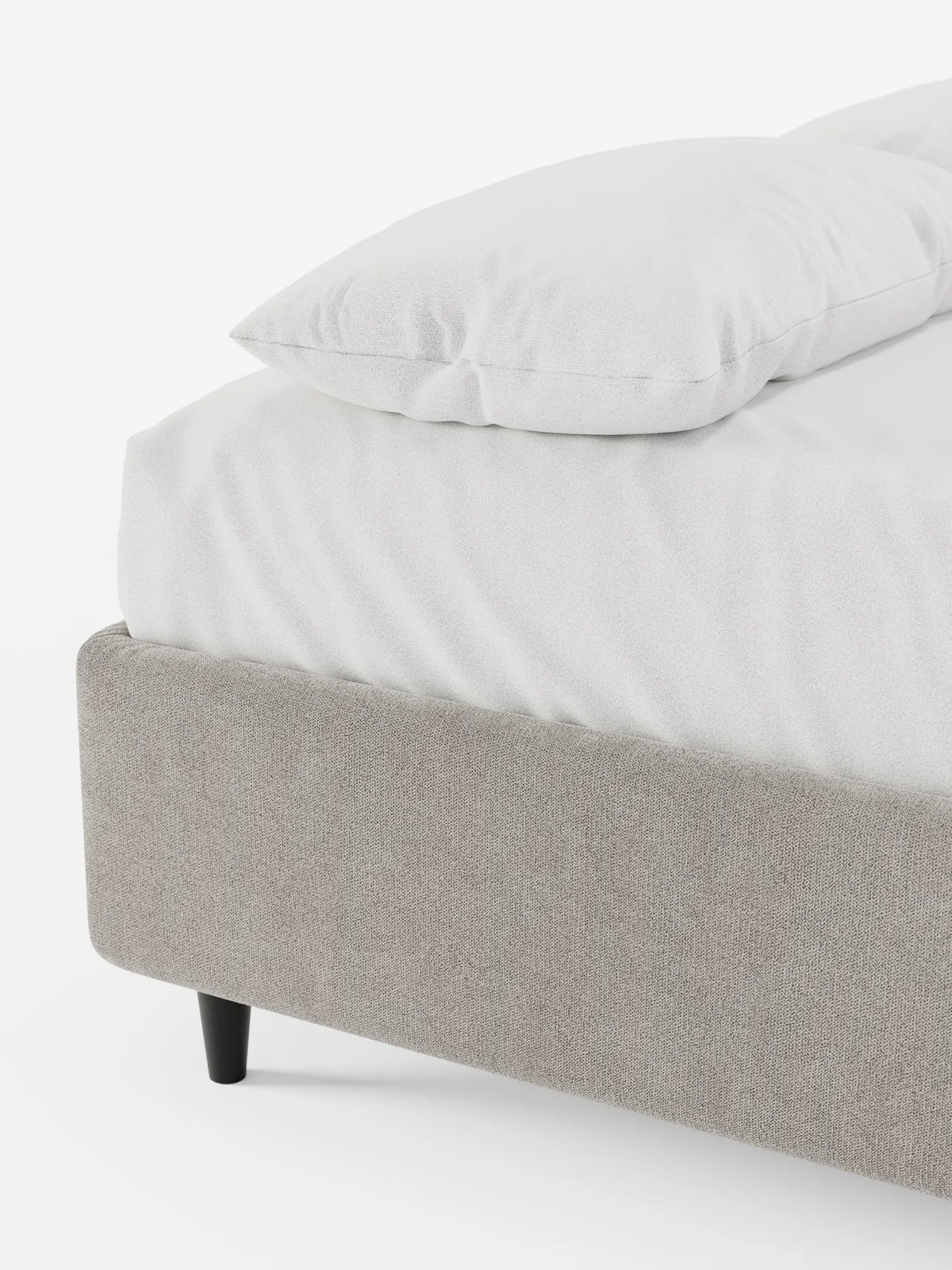 Una vista angolare di un letto sommier ERON grigio chiaro imbottito con vano contenitore in tessuto impermeabile certificato Oeko-Tex, con piedini scuri e affusolati, rivestito con lenzuola bianche e un cuscino coordinato su uno sfondo bianco a tinta unita.
