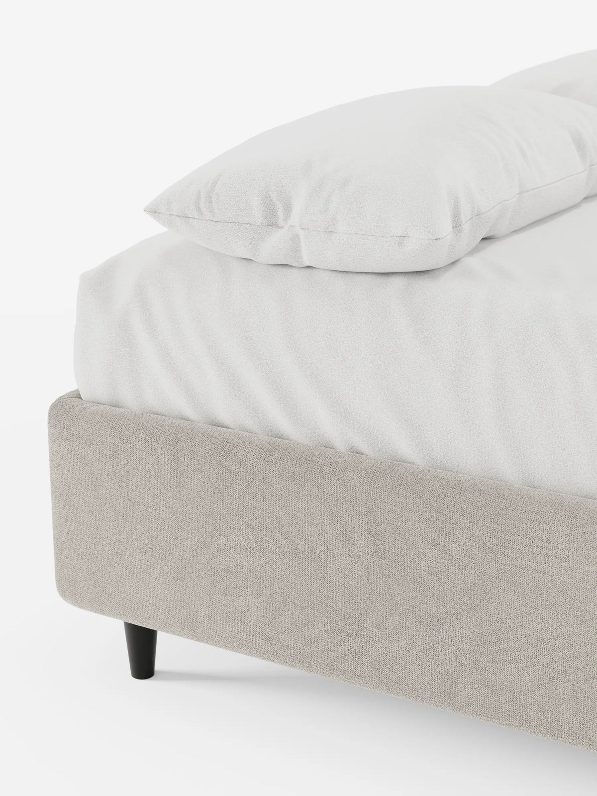 Un primo piano dell'angolo di un letto sommier imbottito ERON color beige chiaro con contenitore, rivestito in tessuto impermeabile certificato Oeko-Tex, adornato con lenzuola bianche e un cuscino, su una gamba corta, scura e affusolata, su uno sfondo bianco.