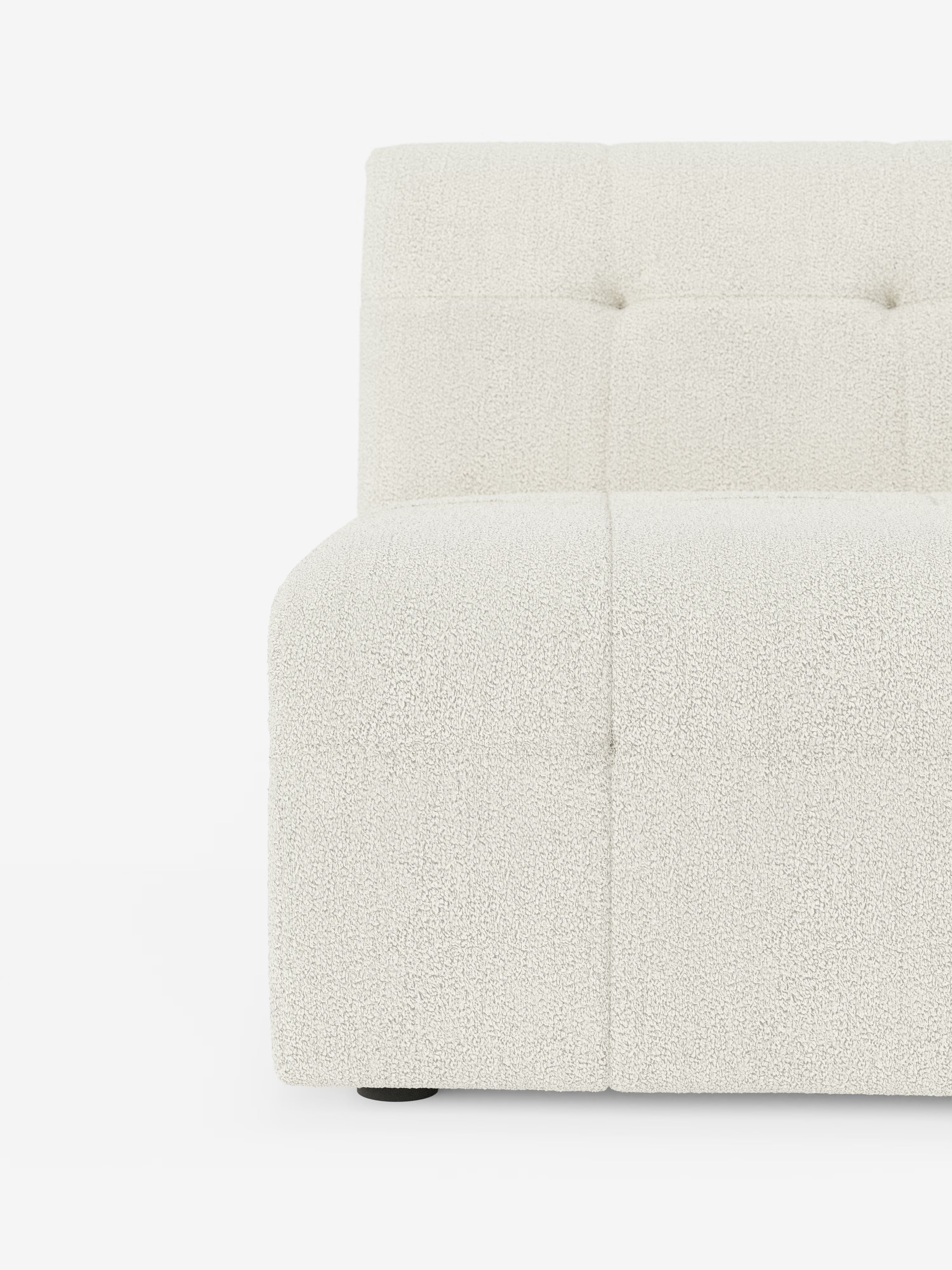 Un primo piano della poltrona Mosaic modulo da 77 cm in bouclé di Divani.Store rivela un divano moderno, bianco e dalla trama ricca, privo di braccioli, caratterizzato da dettagli capitonné sullo schienale e sulla seduta che ne esaltano il design raffinato. Solo la metà sinistra di questo lussuoso divano è visibile su uno sfondo bianco a tinta unita, mettendo in risalto il suo sontuoso tessuto T21 resistente alle macchie e il morbido rivestimento in bouclé.
