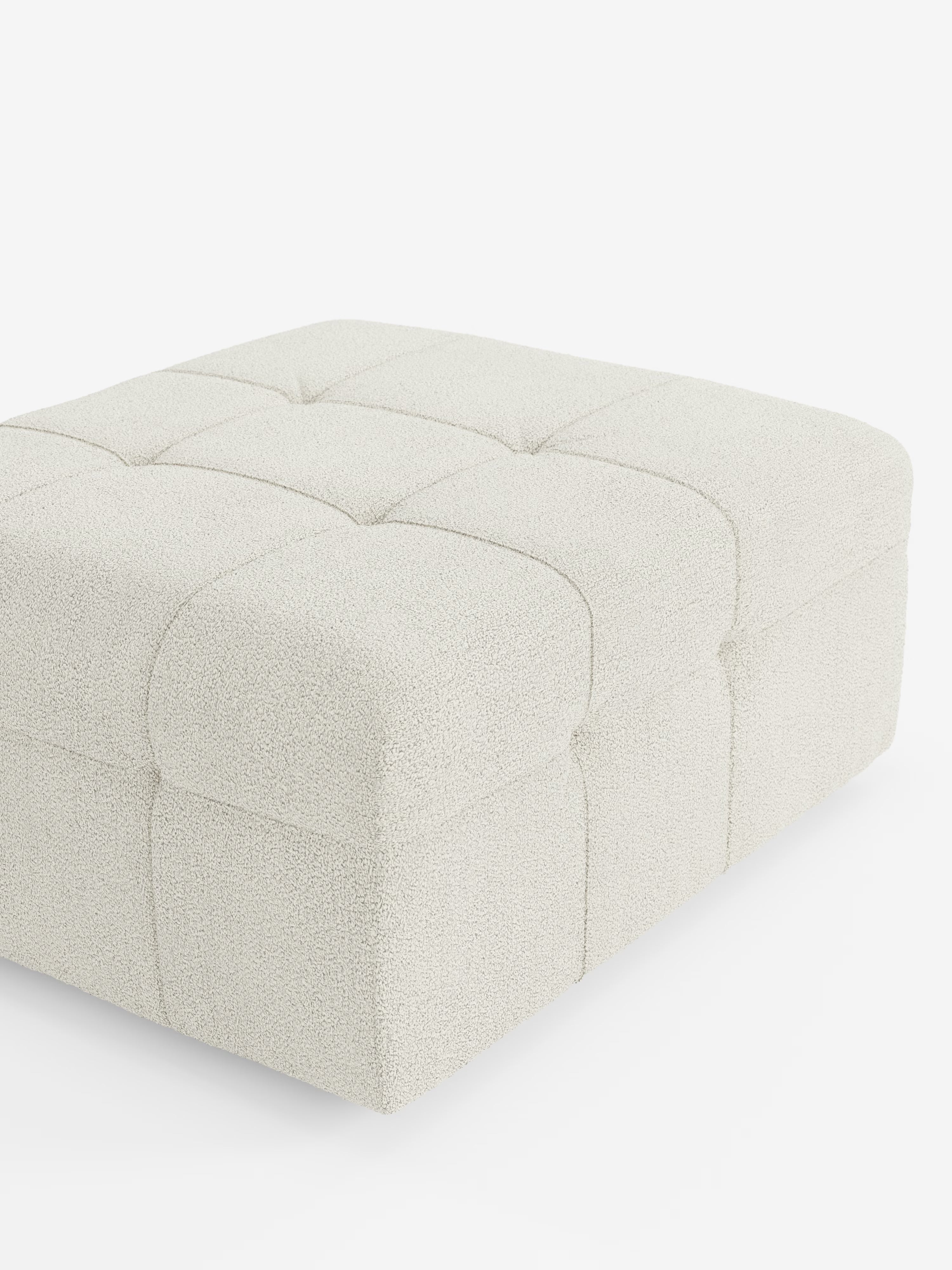 Il pouf e modulo Mosaic in bouclé di Divani.Store è un ampio pouf quadrato (96x77 cm) caratterizzato da un elegante design capitonné con tessuto T21 antimacchia. La sua superficie color avorio, dalla trama rigata, è suddivisa in sei quadrati da sottili cuciture, ciascuno impreziosito da un bottone centrale, che evoca la raffinatezza senza tempo dell’artigianato italiano. Il pouf, morbido e soffice, risalta con grazia sullo sfondo bianco a tinta unita.