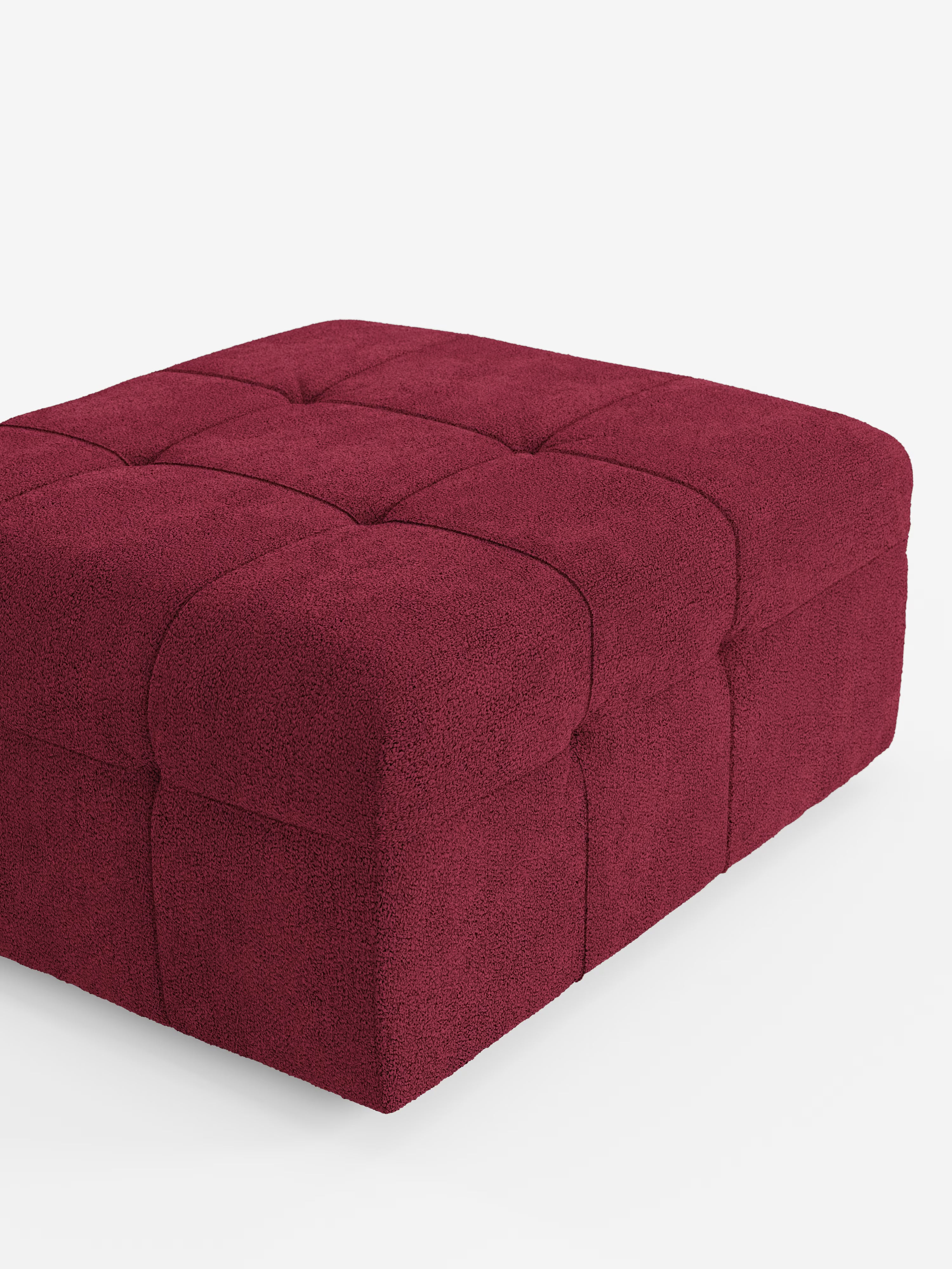 Un pouf quadrato “Mosaic” di Divani.Store, delle dimensioni di 96x77 cm, rivestito in tessuto bouclé T21 antimacchia con motivo capitonné (a bottoni). La superficie testurizzata presenta quadrati cuciti sulla parte superiore e sui lati. Il pouf è raffigurato parzialmente su uno sfondo bianco a tinta unita.