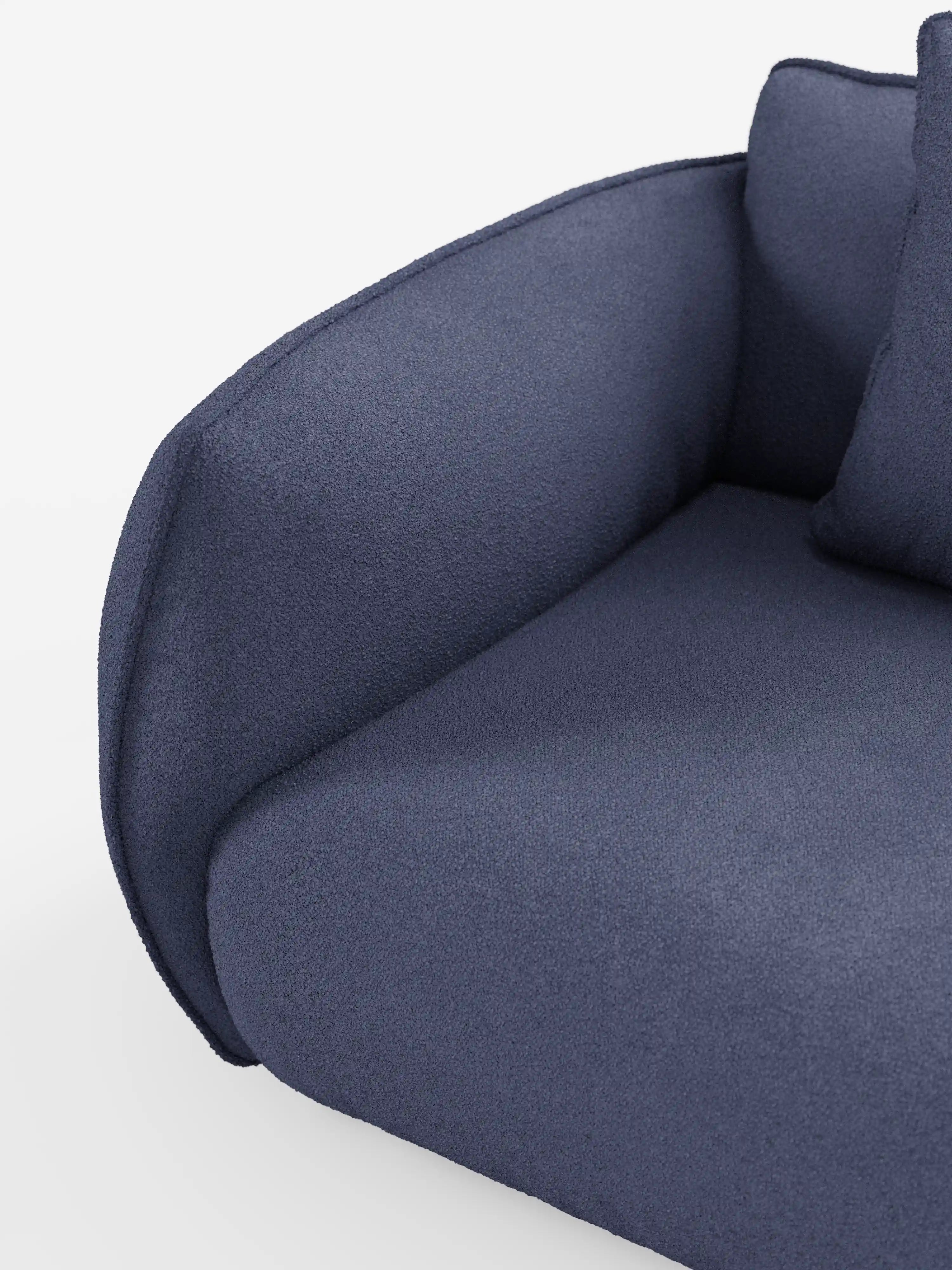 Primo piano del divano modulare a 3 posti “Nimbus” di Divani.Store, rivestito in morbido tessuto T33 effetto cotone, resistente alle macchie, in blu navy. Il moderno design angolare presenta bordi delicatamente arrotondati e un bracciolo imbottito, con un tessuto dall’aspetto testurizzato. Un cuscino coordinato è parzialmente visibile sul lato destro, su uno sfondo bianco a tinta unita.