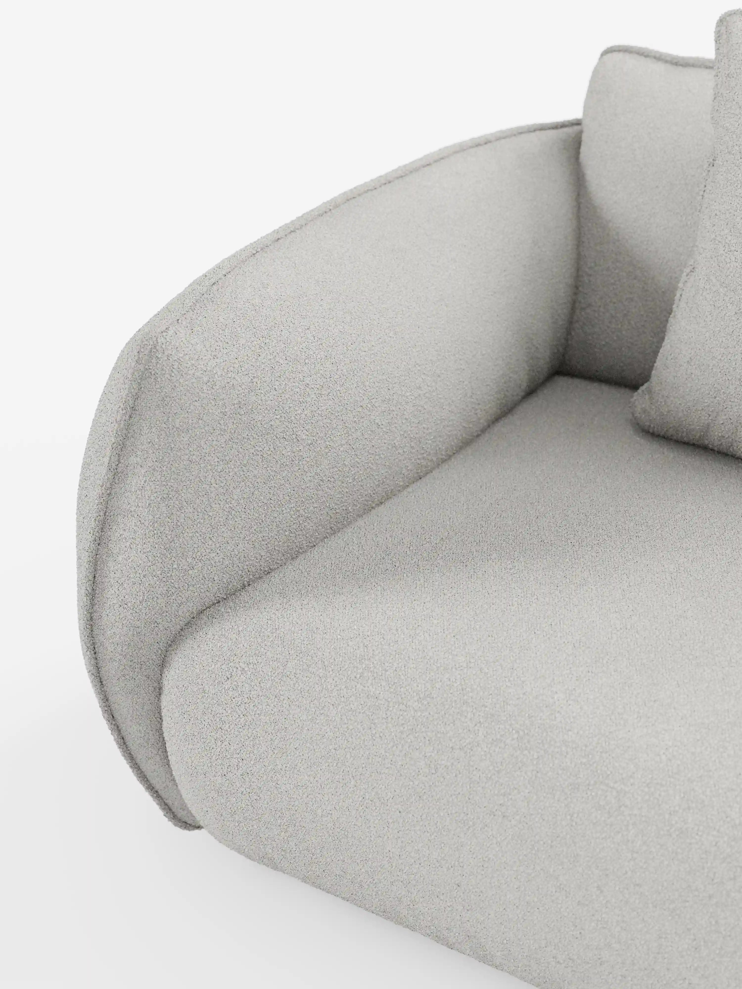 Primo piano del bracciolo e della seduta del divano modulare a 3 posti Nimbus di Divani.Store. Il tessuto T33 grigio chiaro, smacchiabile ed effetto cotone, appare ruvido al tatto e morbido, con bordi puliti e arrotondati e un design minimalista. È visibile una parte del cuscino dello schienale. Lo sfondo bianco a tinta unita mette in risalto le linee morbide del divano.