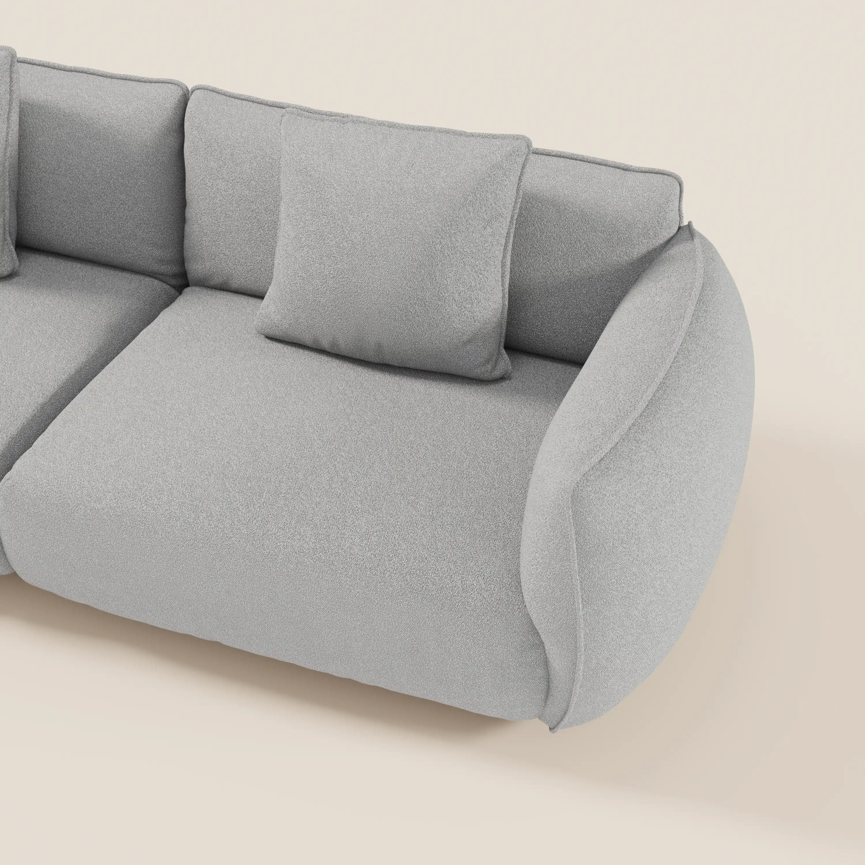 Il divano Nimbus 3 posti modulare e componibile di Divani.Store, 250 cm in smacchiabile tessuto effetto cotone t33, presenta un design grigio chiaro con bordi arrotondati, cuscini in peluche, cuscino quadrato e bracciolo curvo imbottito su sfondo beige chiaro.