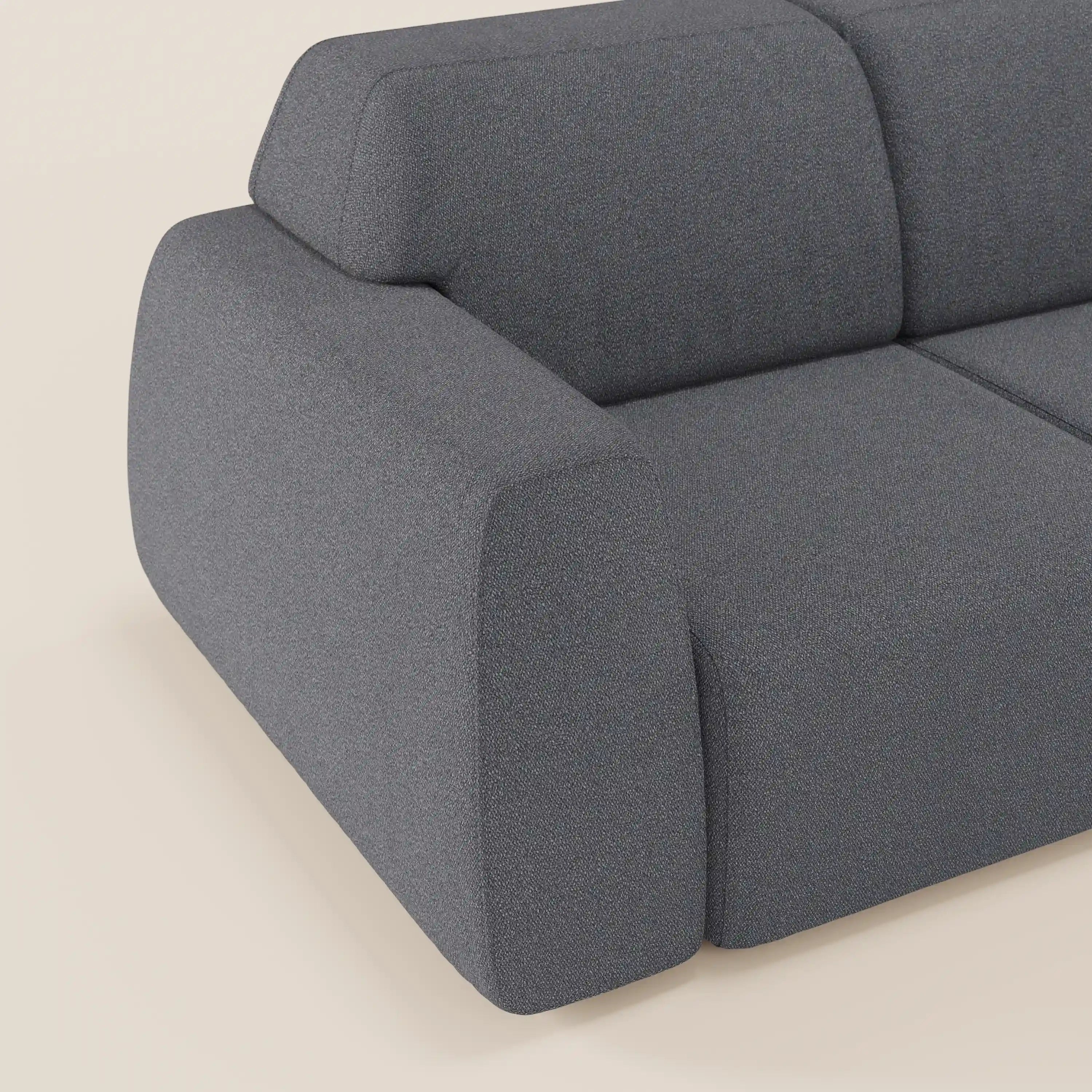 Primo piano del braccio e dello schienale del divano angolare Orbit con penisola reversibile di Divani.Store, caratterizzato da tessuto grigio scuro lavabile effetto cotone T33, bordi arrotondati e design minimalista a blocchi su sfondo beige chiaro.