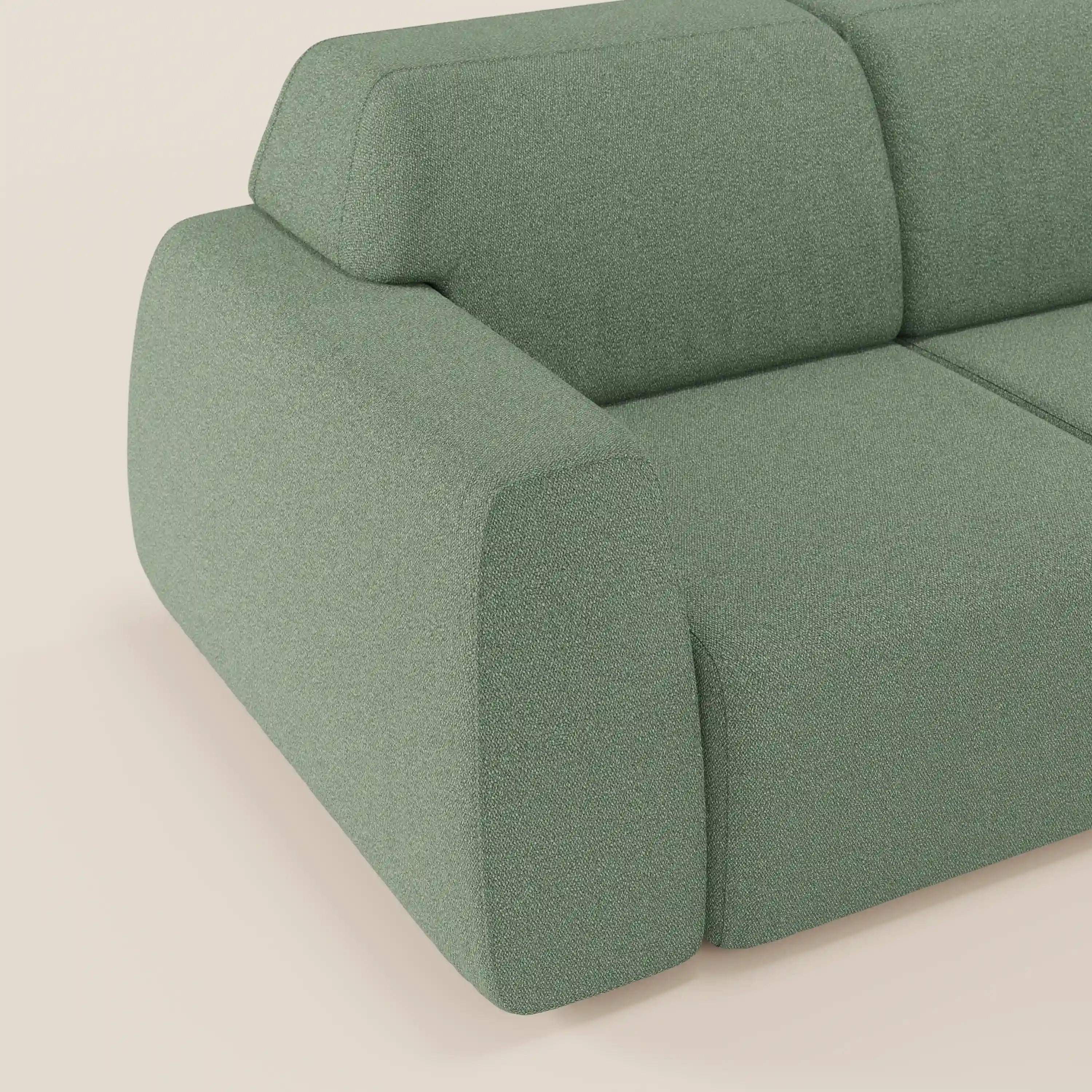 Primo piano del divano angolare Orbit con penisola reversibile di Divani.Store, in tessuto effetto cotone verde T33 smacchiabile, con ampi braccioli e schienale sagomati, su un pavimento chiaro e su un morbido sfondo beige.