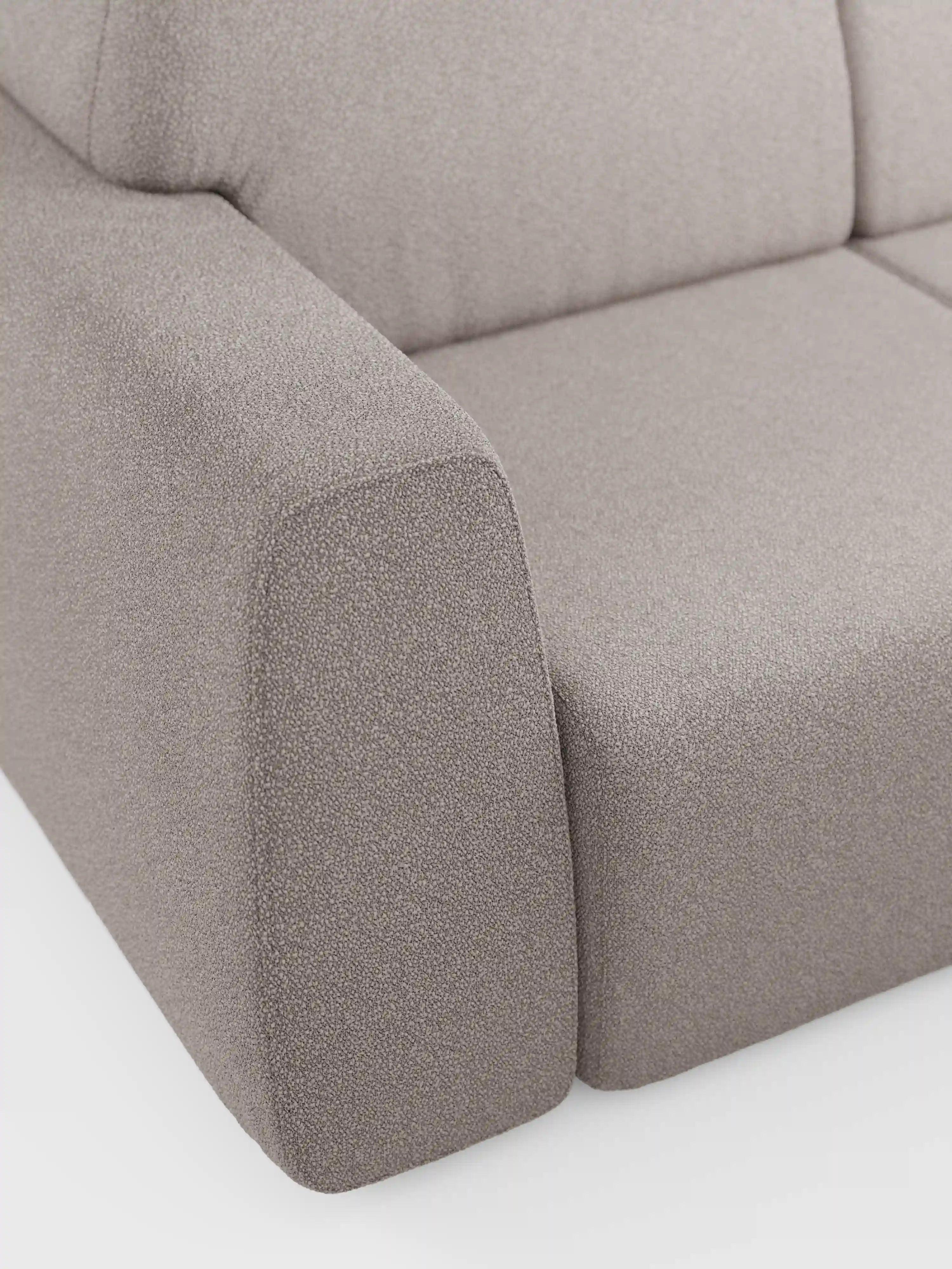 Primo piano del divano a 3 posti Orbit di Divani.Store, che mostra i braccioli e la seduta rivestiti in tessuto T33 grigio chiaro, smacchiabile, effetto cotone. Il rivestimento in tessuto, completamente sfoderabile, presenta un aspetto morbido e materico. Con linee pulite e una silhouette semplice e squadrata, questo divano moderno risalta su uno sfondo bianco a tinta unita. È visibile solo una parte del divano.