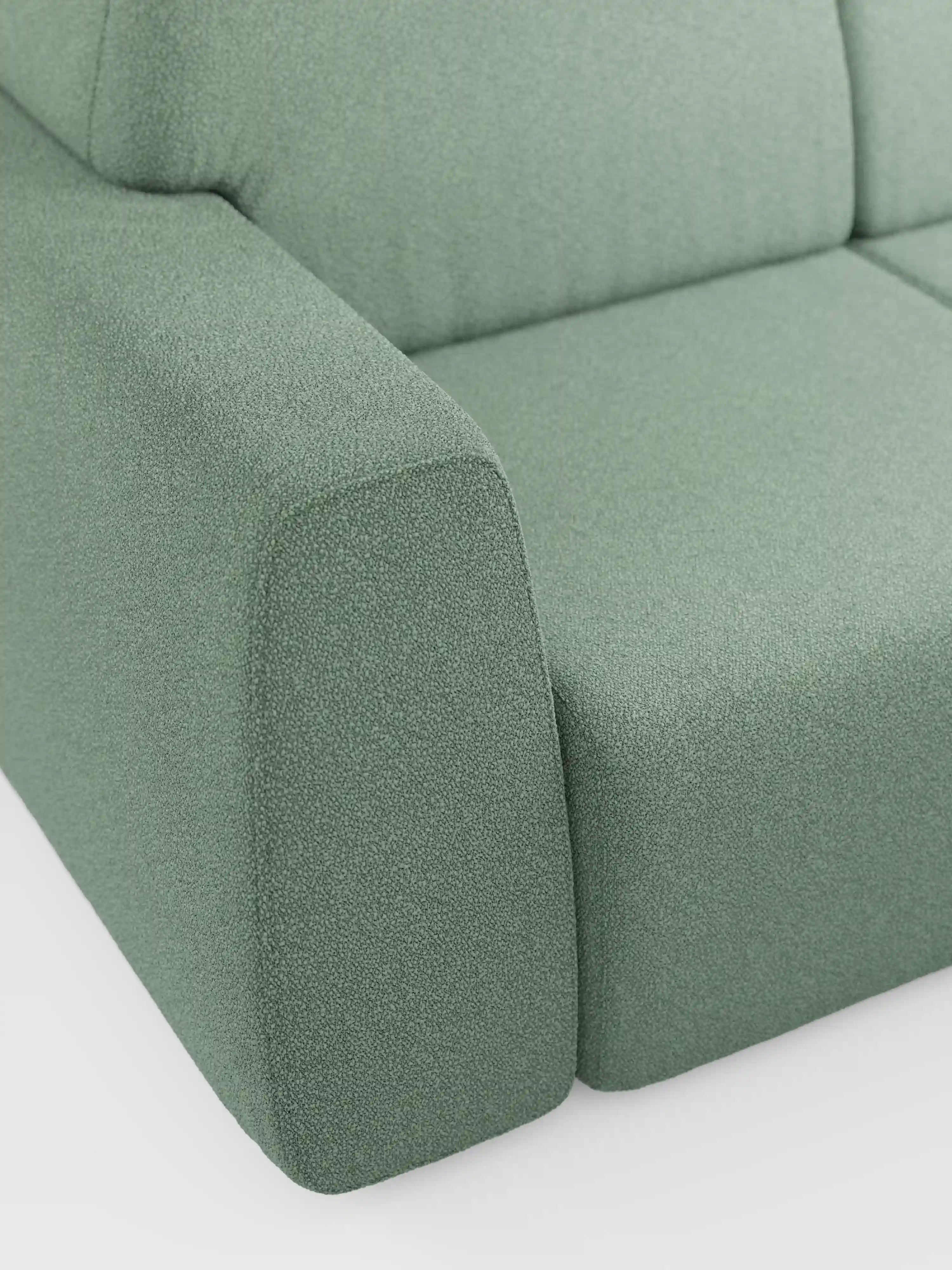 Primo piano del bracciolo e della seduta del divano Orbit a 2 e 3 posti con sedute scorrevoli di Divani.Store, rivestito in tessuto T33 verde salvia testurizzato, effetto cotone e resistente alle macchie. Il design è squadrato, con linee morbide e pulite, e il divano è ripreso su uno sfondo bianco a tinta unita.