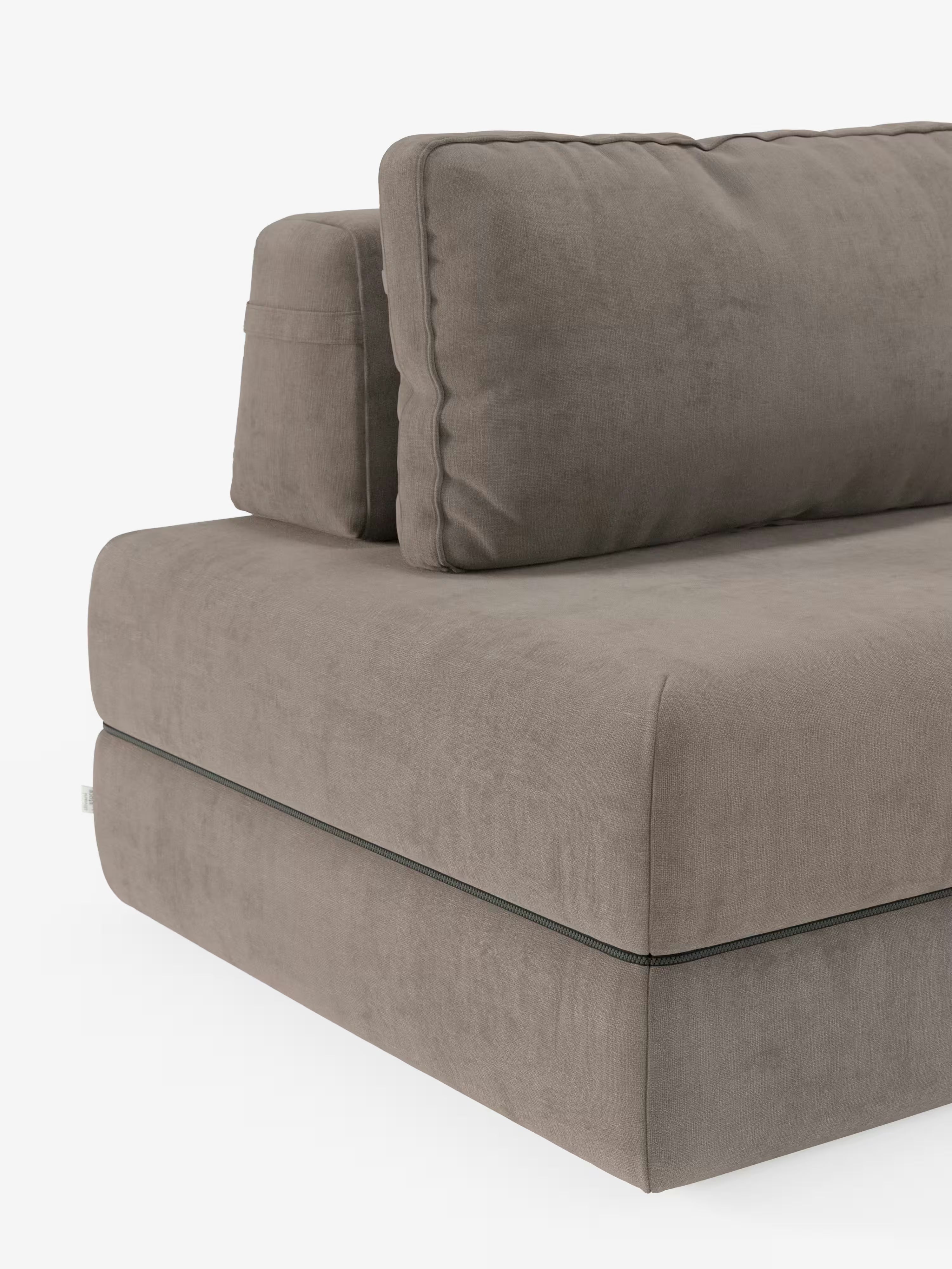 Un primo piano del divano letto matrimoniale Rift di Divani.Store ne mette in risalto la silhouette moderna e rettangolare, rivestita in tessuto T31 grigio talpa resistente alle macchie. L’immagine evidenzia i morbidi cuscini di seduta e schienale con cuciture a vista e gli schienali regolabili, sottolineandone il design minimalista e squadrato. Il divano è posizionato su uno sfondo bianco liscio ed è dotato di un materasso in memory foam alto 24 cm per un comfort ancora maggiore.