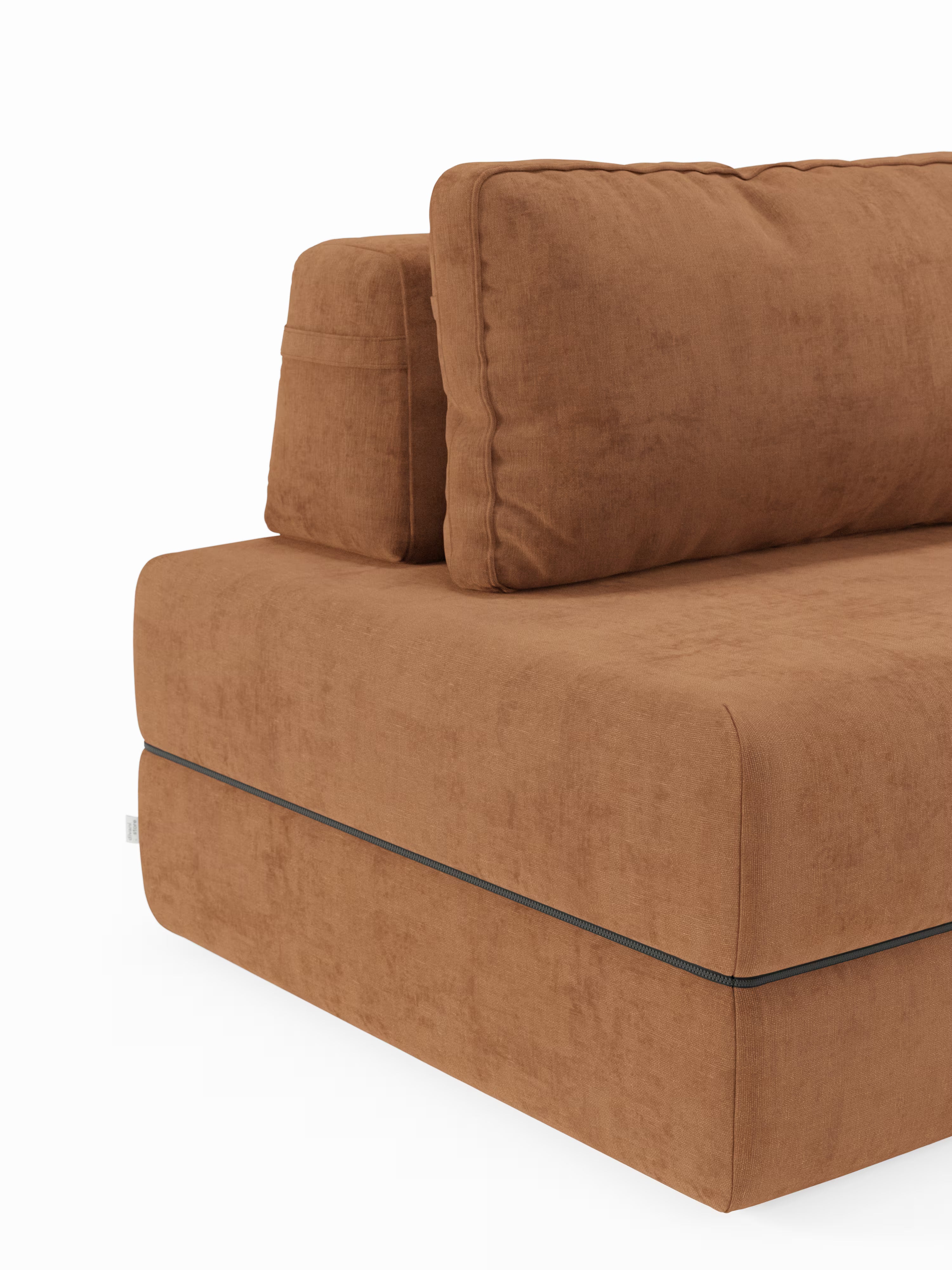Un primo piano della poltrona letto Rift di Divani.Store ne mette in risalto la silhouette moderna e squadrata, con cuscini imbottiti e un morbido tessuto T31 dalla trama scamosciata e resistente alle macchie. L'immagine mette in risalto l'angolo sinistro del divano, caratterizzato da cuciture a vista e da un'imbottitura spessa, tipiche del design contemporaneo. La poltrona letto è dotata di un materasso in memory foam alto 22 cm e di uno schienale regolabile. Lo sfondo è bianco a tinta unita.