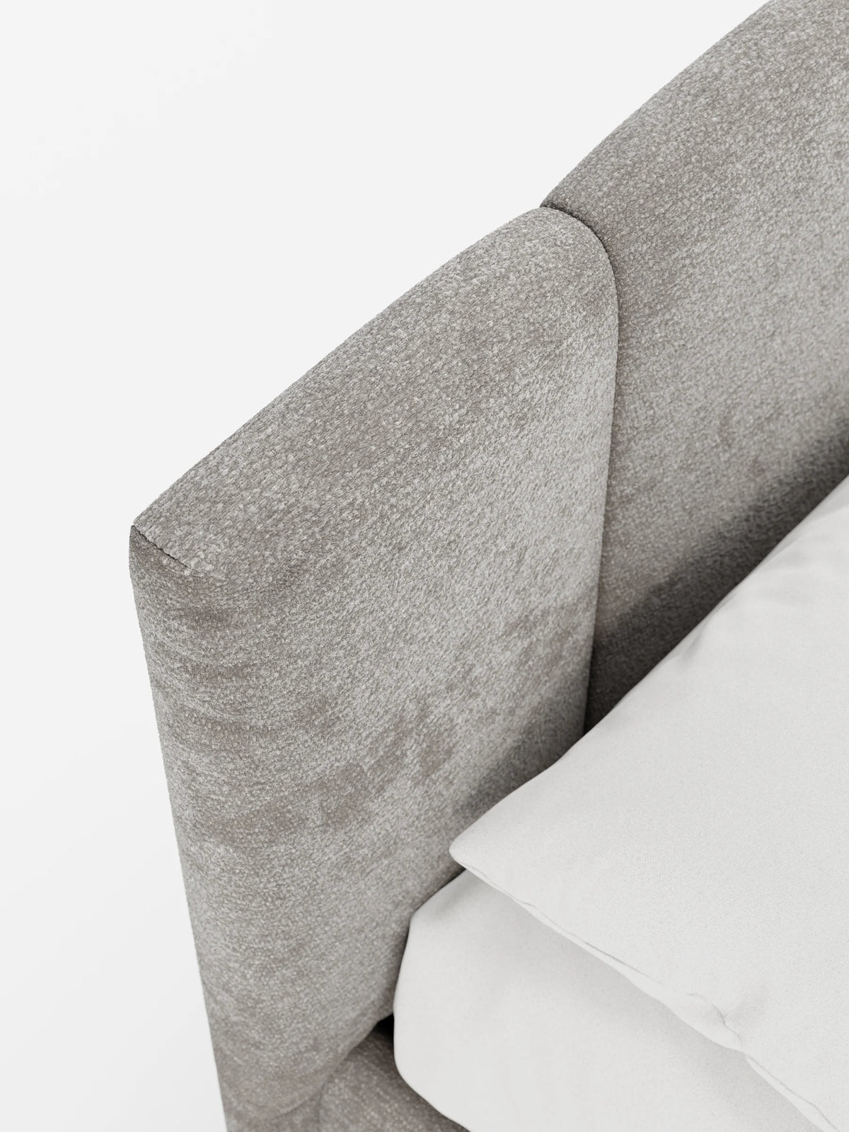 Un primo piano del letto imbottito ARKAM con contenitore e testiera a cuciture verticali, caratterizzato da una testiera imbottita color taupe con cuciture verticali e un cuscino bianco candido su uno sfondo luminoso.