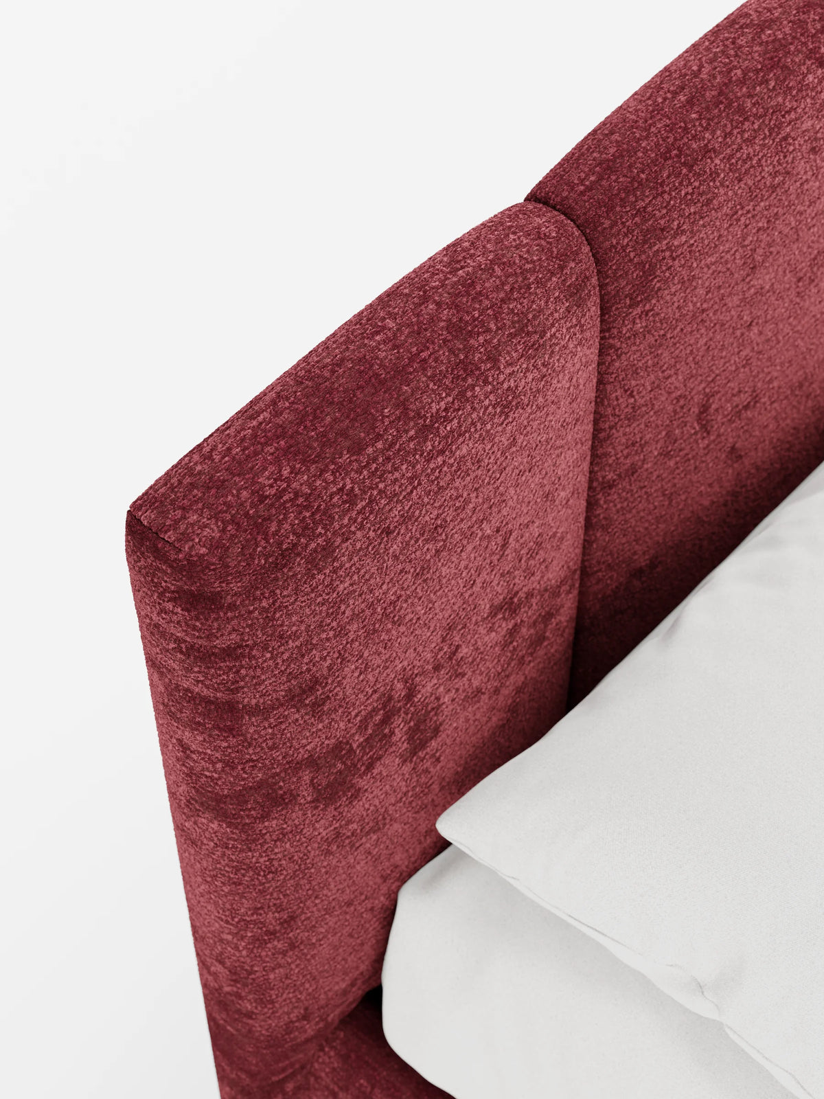 Un primo piano di un divano letto ARKAM di colore rosso intenso e dalla superficie ruvida, dotato di vano contenitore e testiera con lavorazione verticale, su cui è appoggiato un cuscino bianco a tinta unita.