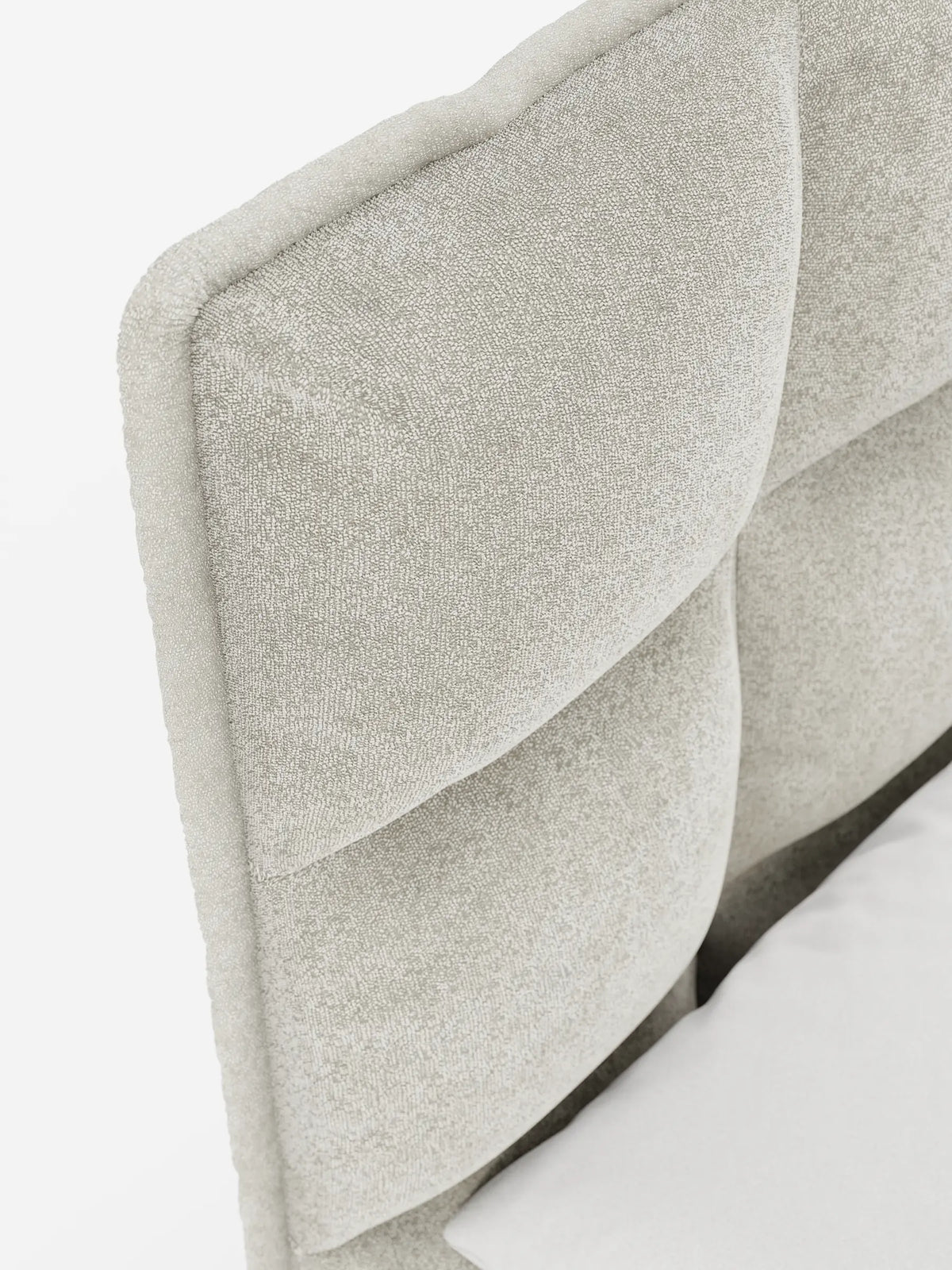 Primo piano del letto imbottito AURO con contenitore e testiera capitonné alta in ciniglia Oeko-Tex®, caratterizzato da una testiera beige a pannelli quadrati trapuntati con una delicata lucentezza, inquadrata dall’angolo di un lenzuolo bianco.