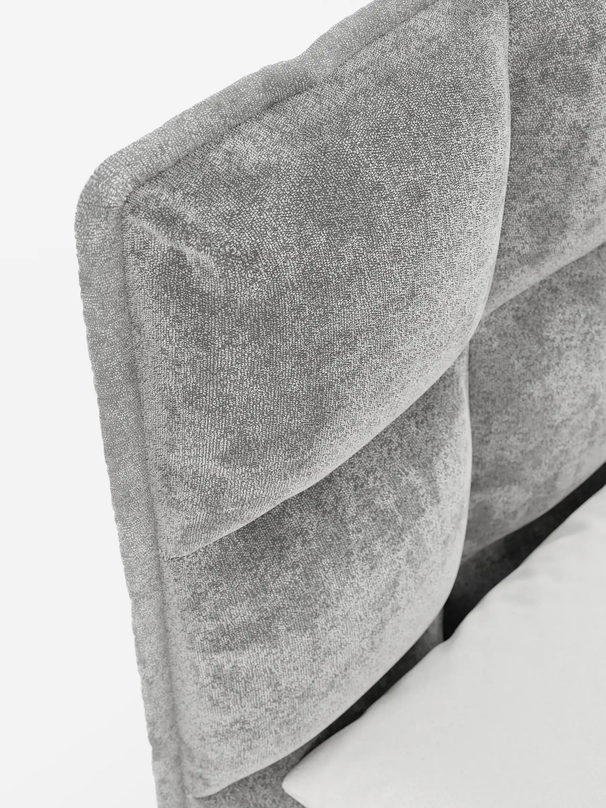 Un primo piano del letto imbottito AURO con contenitore e testiera capitonné alta in ciniglia Oeko-Tex®, caratterizzato da ampie sezioni quadrate imbottite in tessuto grigio chiaro testurizzato, con un cuscino bianco visibile in basso a destra.