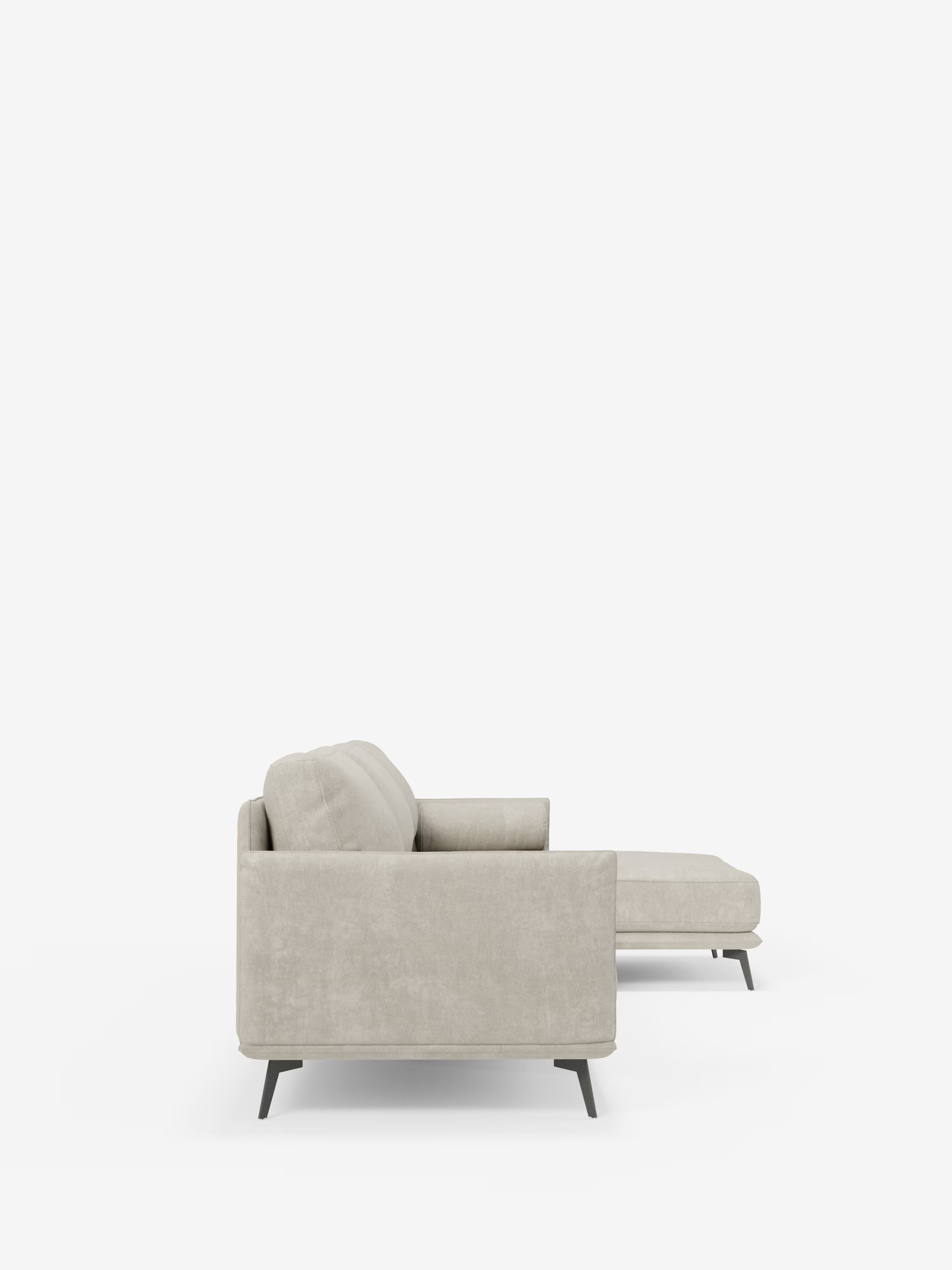 Vista laterale del divano moderno angolare con penisola “Basalto” di Divani.Store, qui presentato in tessuto T31 grigio chiaro e antimacchia. Questo divano presenta una silhouette moderna con un’elegante base in metallo, braccioli bassi e squadrati e una chaise longue orientata verso destra. I cuscini in piuma aggiungono comfort alle linee pulite e al design minimalista, il tutto su uno sfondo bianco a tinta unita che ne sottolinea l’estetica contemporanea.