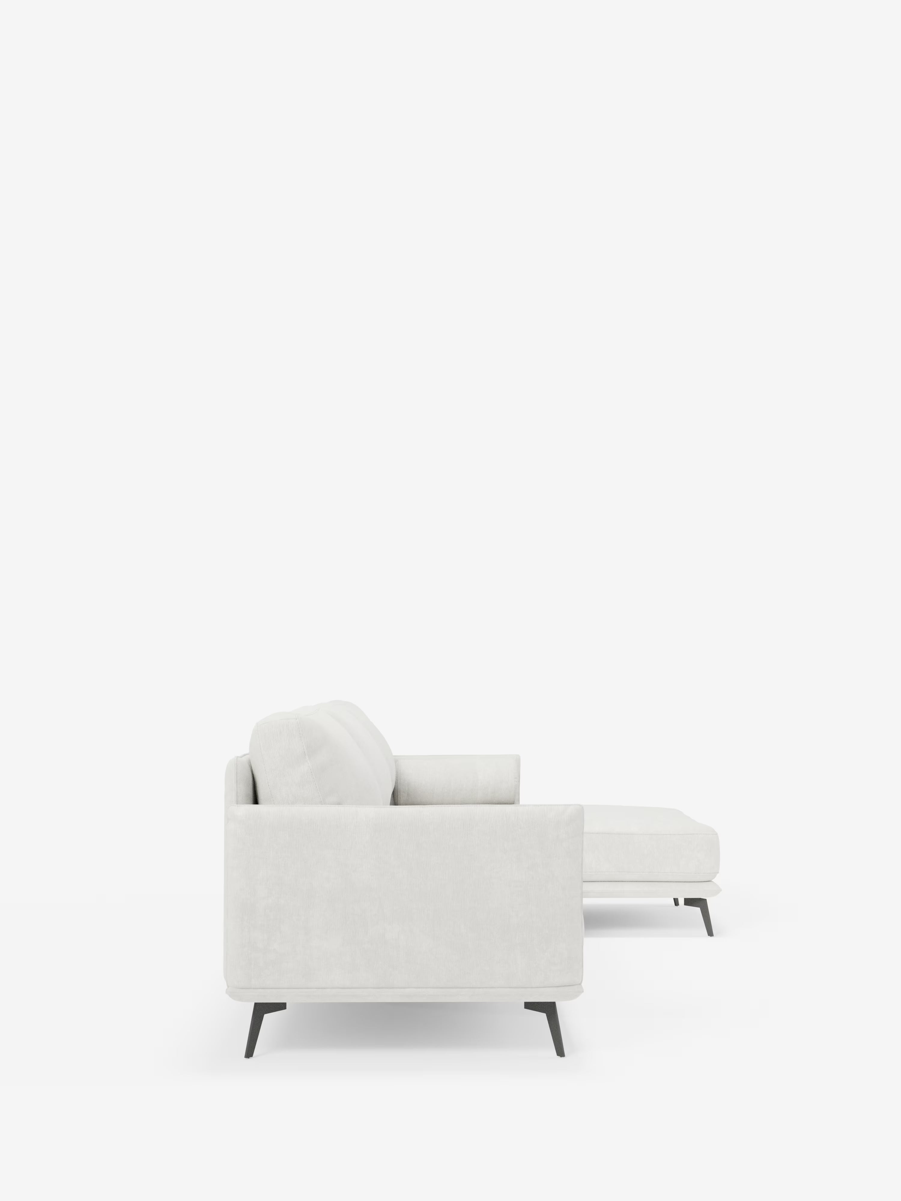 Vista laterale del divano moderno angolare con penisola "Basalto" di Divani.Store, in tessuto smacchiabile T31 grigio chiaro, dotato di chaise longue sul lato destro. Questo divano moderno presenta linee pulite, braccioli squadrati e poggia su un'elegante base in metallo con quattro gambe sottili e angolate di colore nero. I cuscini in piuma aggiungono ulteriore comfort. Lo sfondo è bianco a tinta unita, senza decorazioni o elementi circostanti visibili.