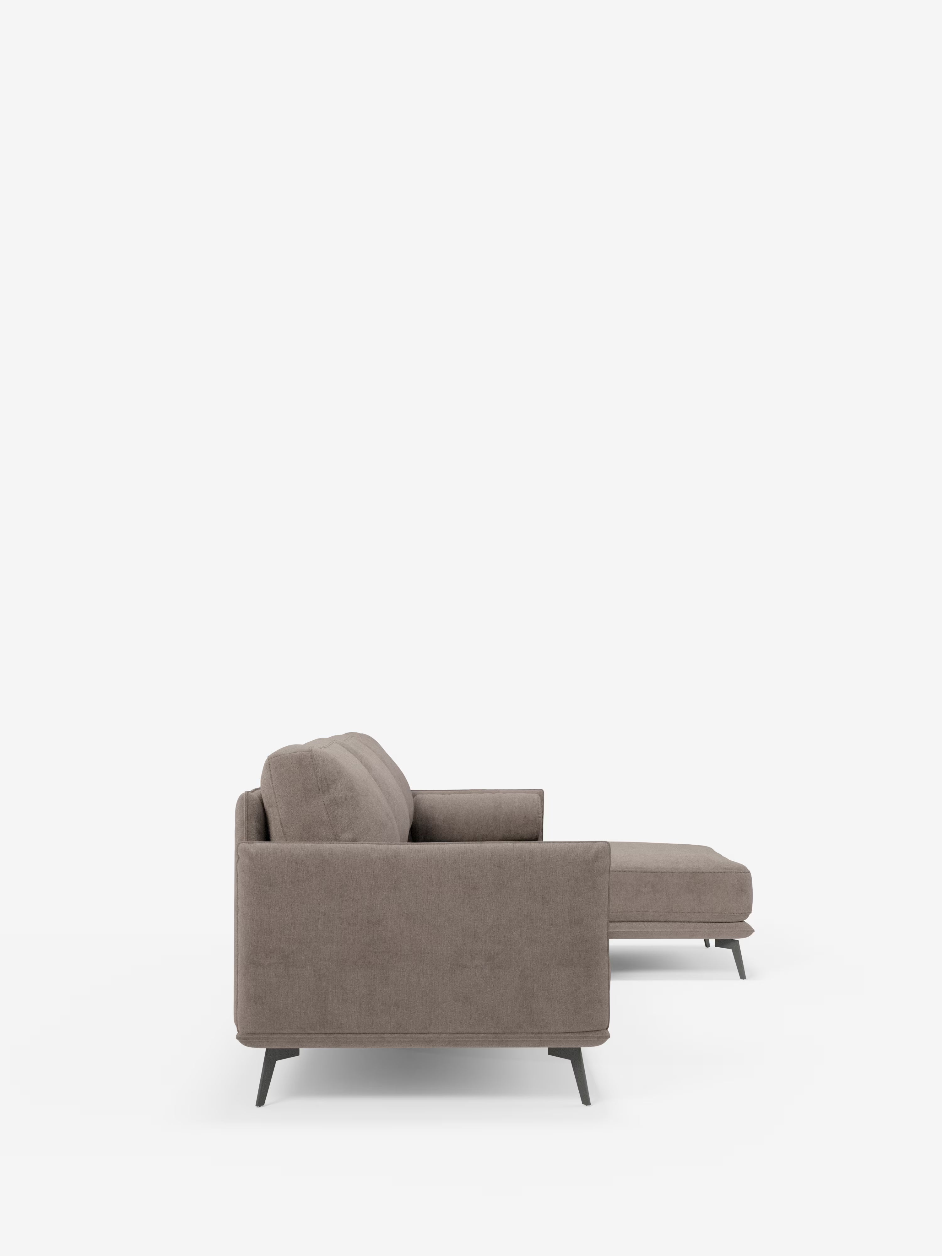 Vista laterale del divano moderno angolare con penisola “Basalto” di Divani.Store, in tessuto T31 marrone chiaro e resistente alle macchie. Questo divano componibile si caratterizza per le linee pulite, un bracciolo sinistro, morbidi cuscini dello schienale e della seduta imbottiti in piuma e sottili gambe in metallo nero. La sezione chaise longue si estende verso destra su uno sfondo bianco a tinta unita.