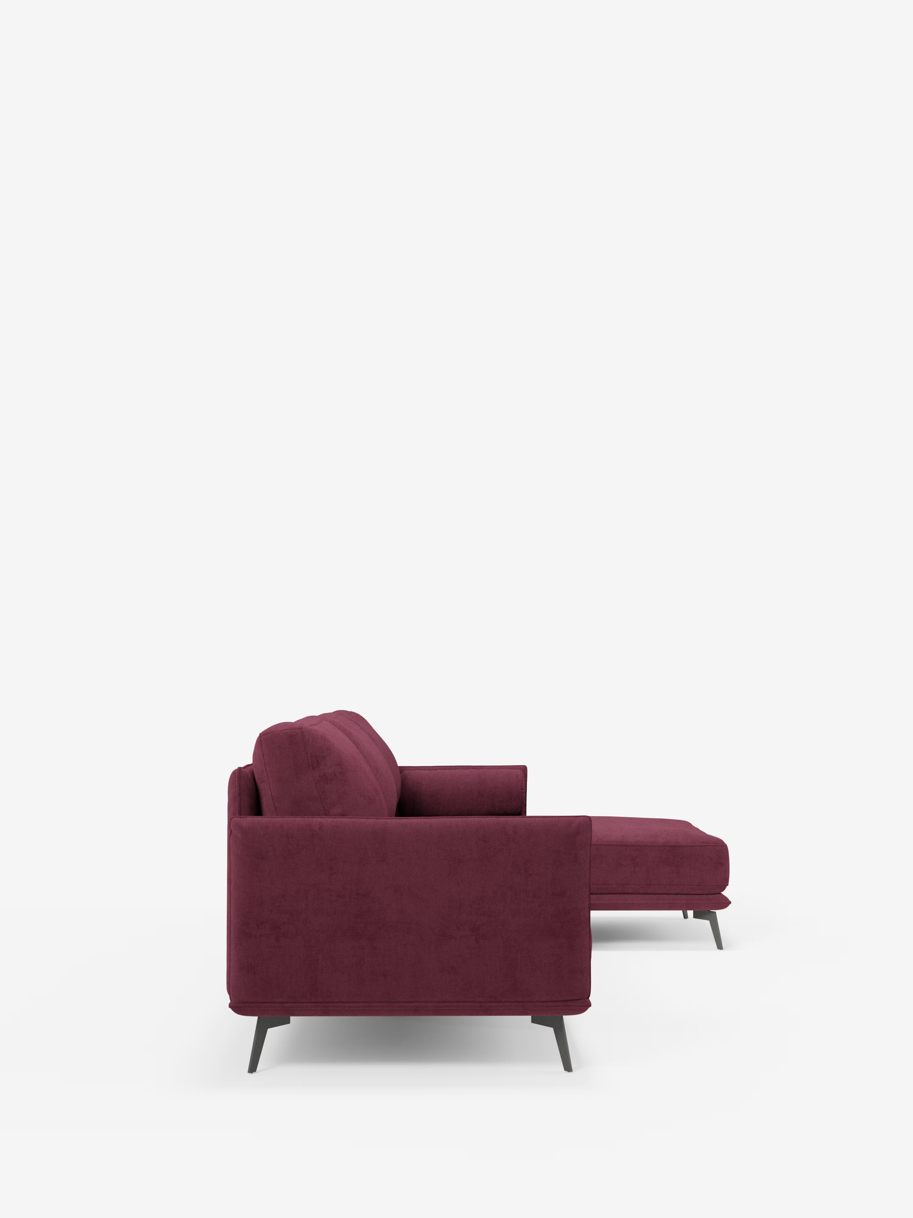 Il divano moderno angolare con penisola Basalto di Divani.Store è qui raffigurato di profilo in tessuto T31 color bordeaux intenso, resistente alle macchie. Questo elegante divano presenta una base in metallo dalle linee slanciate, morbidi cuscini in piuma, linee pulite, un bracciolo sinistro, gambe angolate di colore scuro e una chaise longue estesa sulla destra. Lo sfondo è a tinta unita e di colore chiaro.