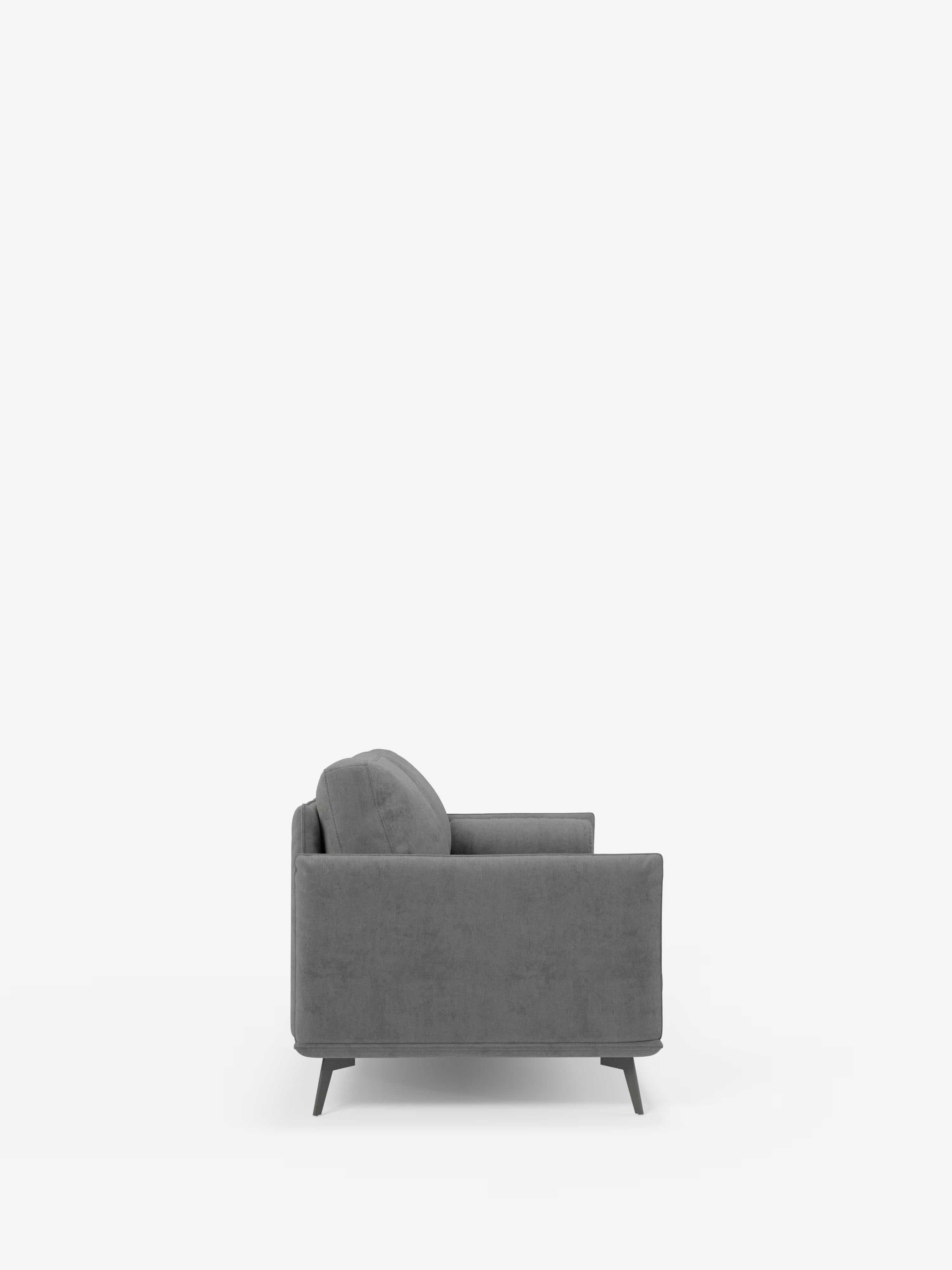 Una poltrona grigia in stile contemporaneo della collezione “Basalto Divano lineare” di Divani.Store è raffigurata di profilo su uno sfondo bianco a tinta unita. Ispirata al design minimalista italiano, la poltrona presenta braccioli dritti e gambe sottili in metallo, con schienale e seduta costituiti da un unico cuscino realizzato in tessuto T31 di facile pulizia, per un look elegante e lineare.