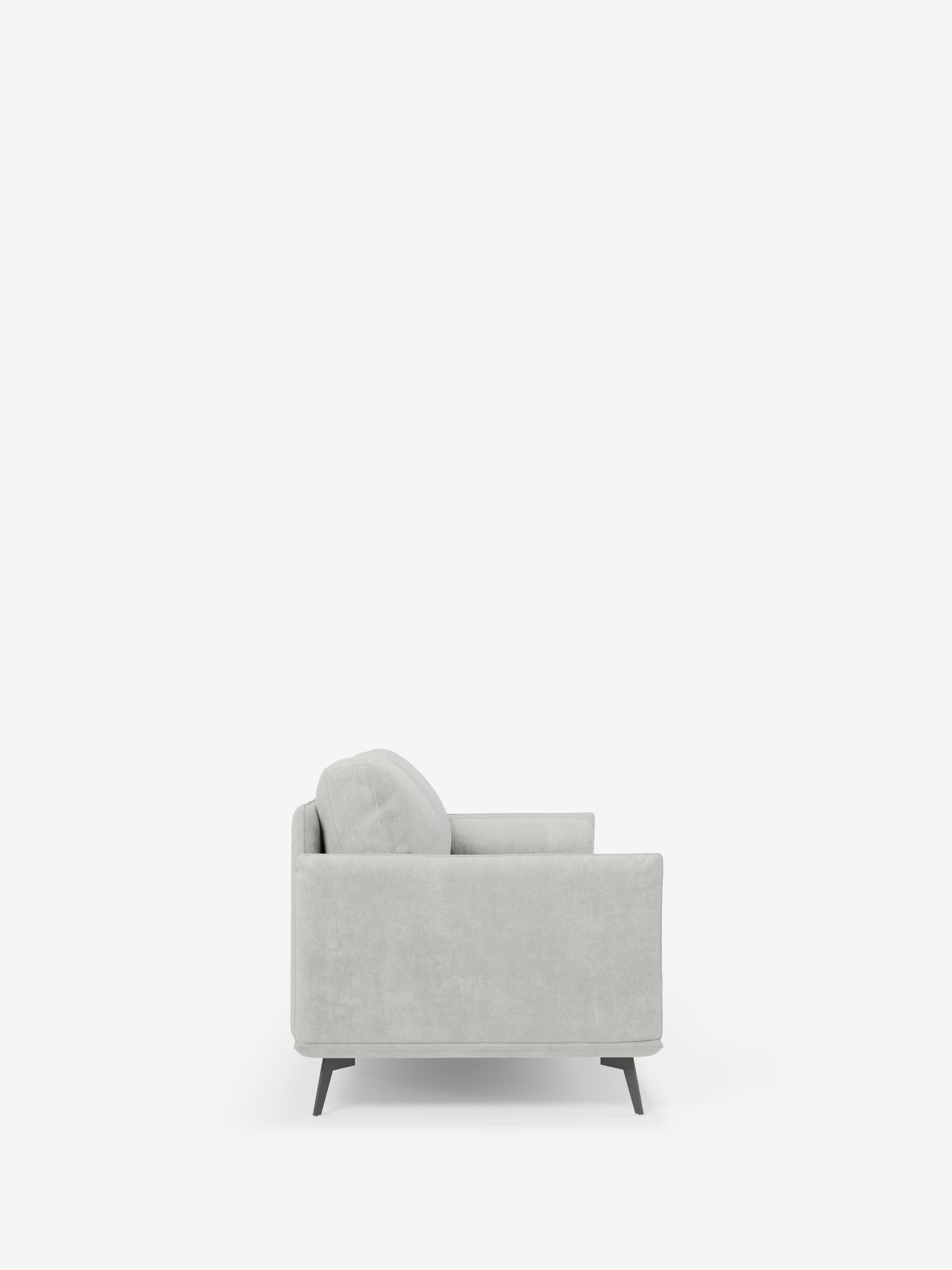 Vista laterale del divano lineare a 2 posti “Basalto” di Divani.Store in grigio chiaro, caratterizzato da braccioli sottili, un unico cuscino per seduta e schienale e gambe affusolate in metallo scuro. Questo divano moderno e minimalista, rivestito in tessuto T31 antimacchia, è posizionato al centro di uno sfondo bianco, circondato da ampio spazio libero.