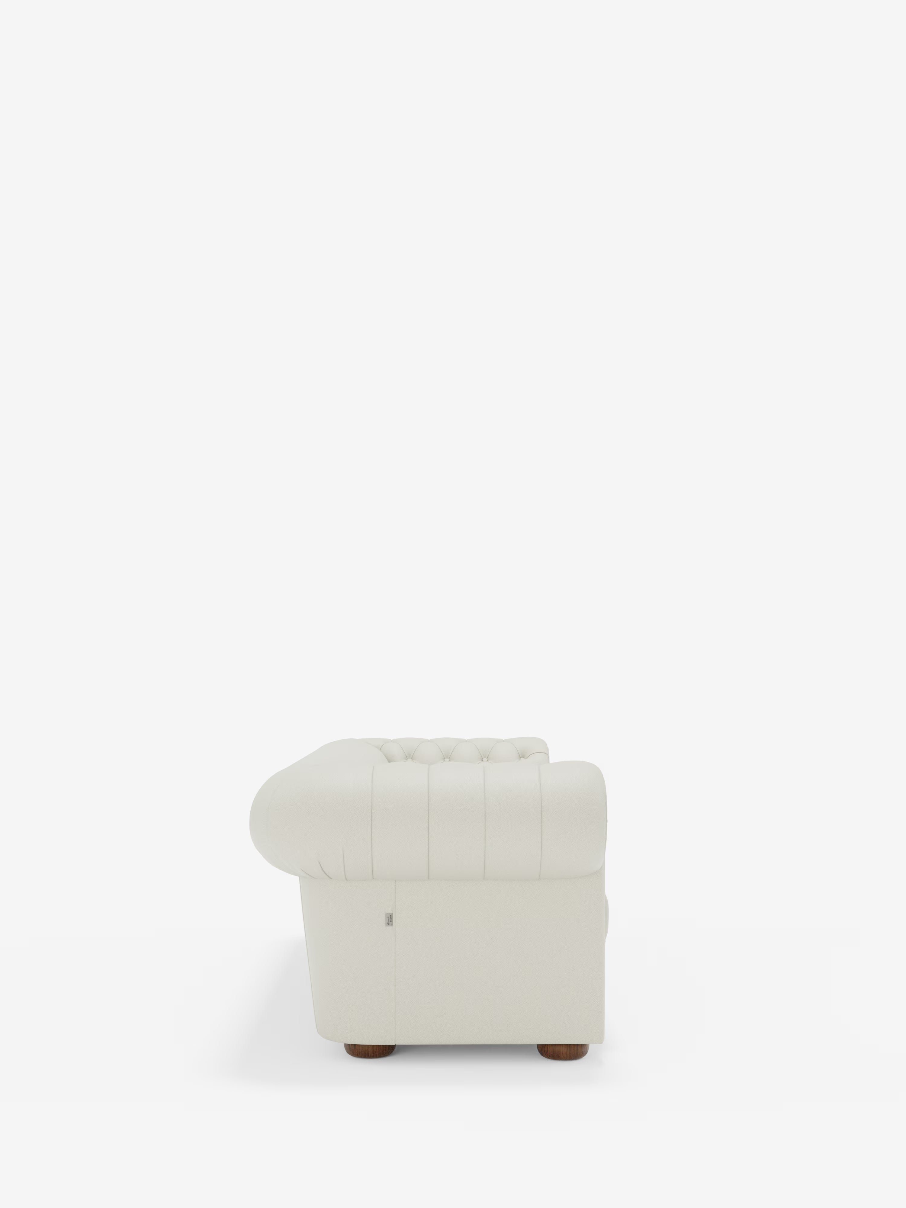 Vista laterale del Chester 4 Posti 3 sedute in Vera Pelle – Chesterfield Capitonné Artigianale di Divani.Store, un divano bianco realizzato artigianalmente con il classico design Chesterfield. Questo divano presenta profondi dettagli a bottoni lungo lo schienale e braccioli arrotondati, rivestiti in morbida vera pelle. Poggia su piccoli piedini rotondi in legno su uno sfondo bianco a tinta unita.