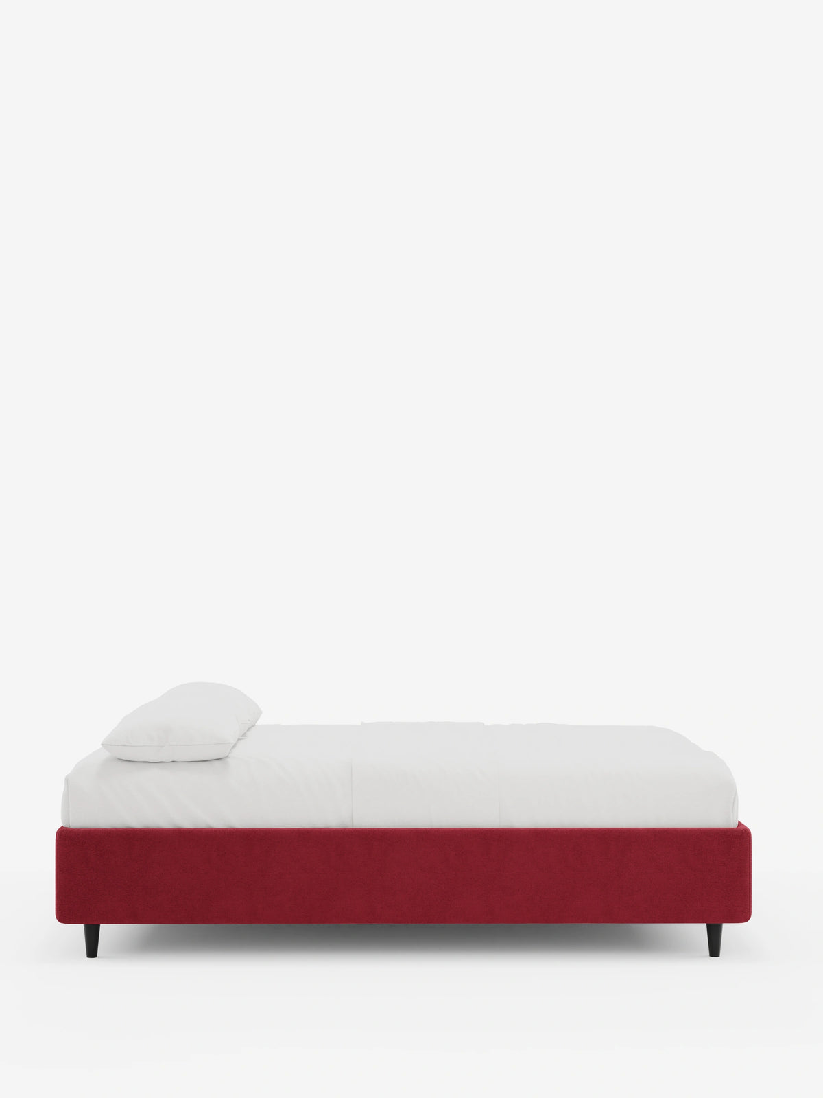 Vista di profilo del letto sommier imbottito ERON con contenitore, rivestito in tessuto impermeabile certificato Oeko-Tex di colore rosso intenso, poggiato su gambe corte e affusolate di colore scuro, con materasso e cuscino bianchi su uno sfondo chiaro e uniforme.