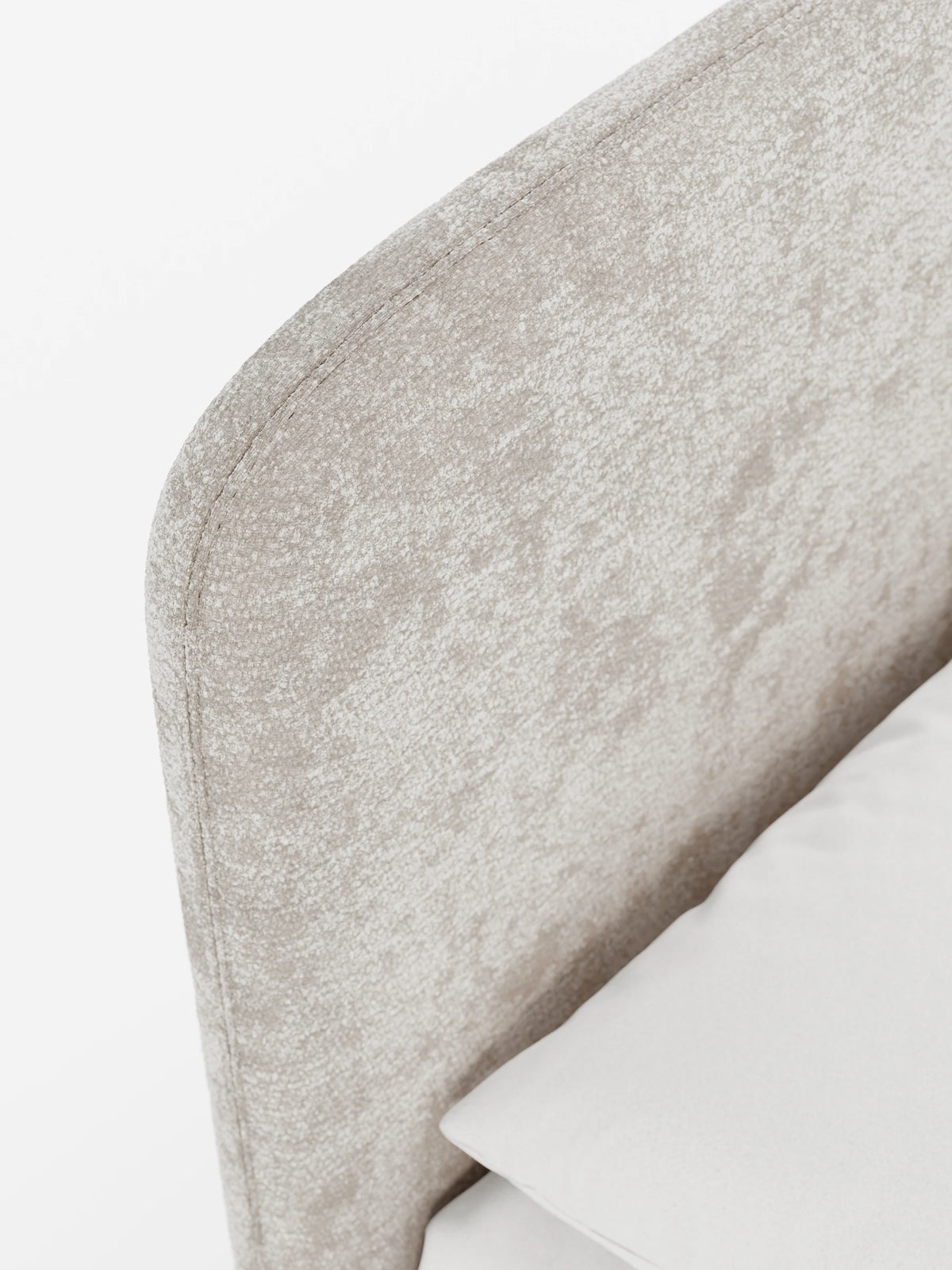 Un primo piano del letto KAELOS minimal imbottito, caratterizzato da una testiera imbottita in tessuto chenille beige chiaro con bordi arrotondati e un unico cuscino bianco su uno sfondo bianco a tinta unita.