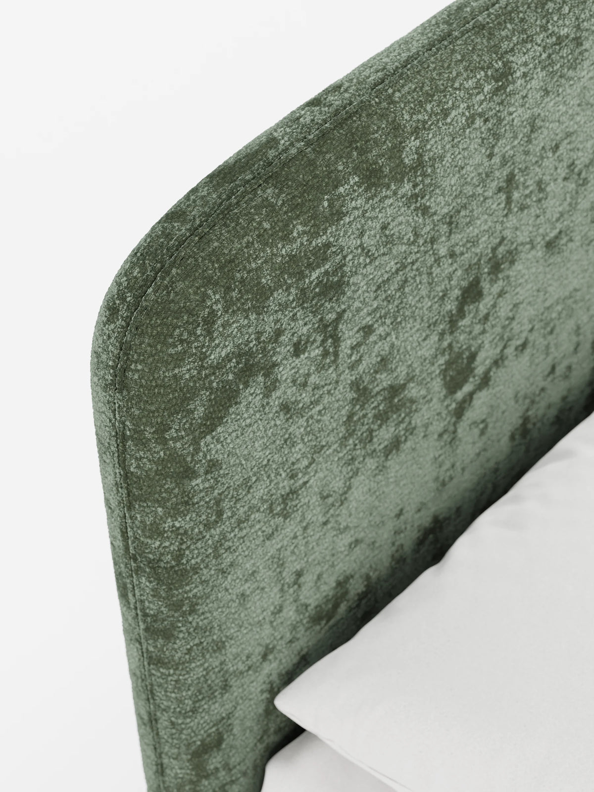 Un primo piano della testiera imbottita KAELOS “letto minimal” di colore verde oliva, con angoli arrotondati e tessuto testurizzato, con un cuscino bianco appoggiato contro di essa.