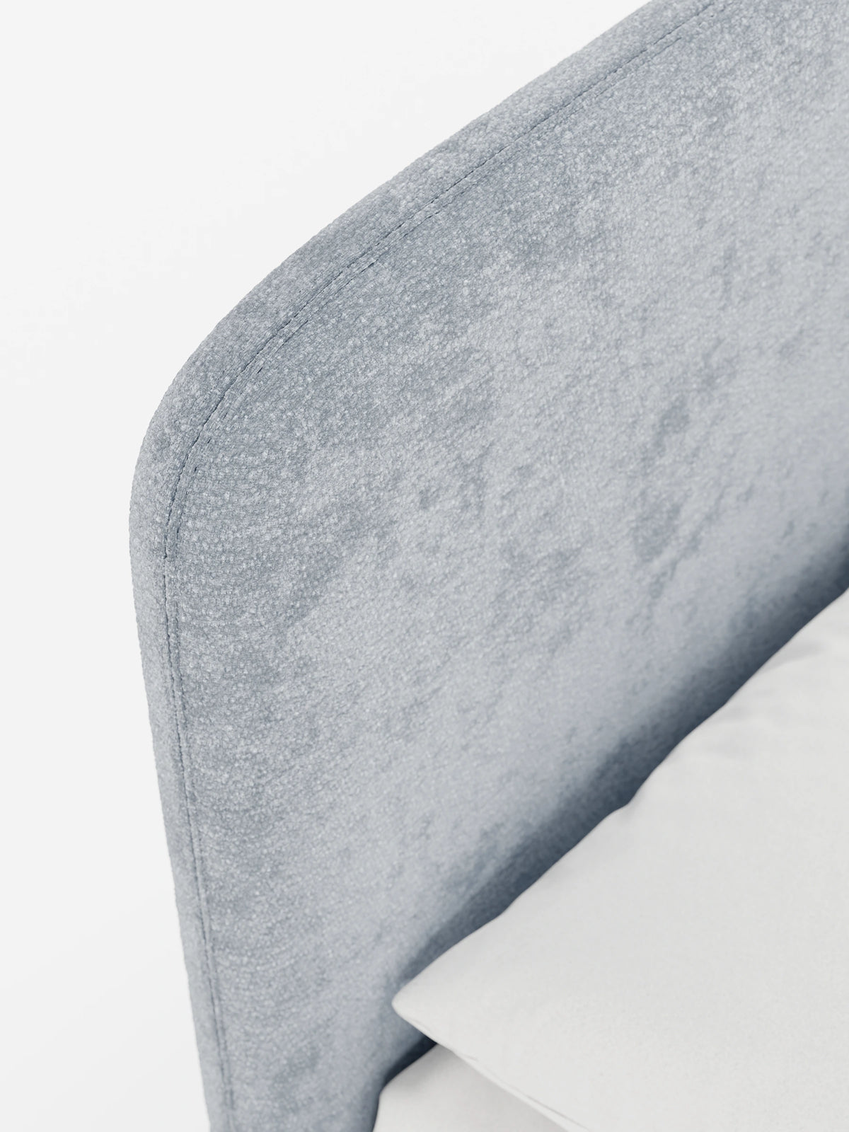 Un primo piano di una testiera imbottita KAELOS Letto Minimal di colore grigio, con finitura in tessuto chenille arrotondata e testurizzata e cuciture curate, raffigurata con un cuscino bianco su uno sfondo a tinta unita.