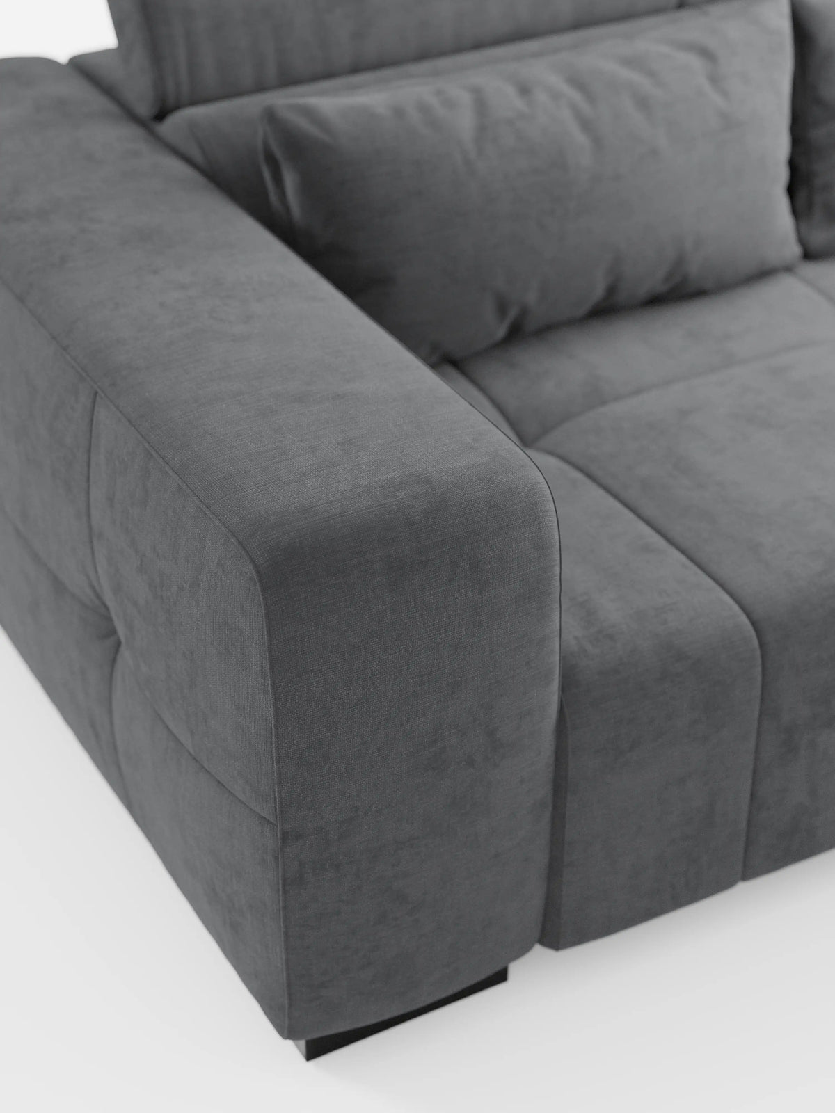 Un primo piano del divano Monarch con relax elettrico per l'allungamento delle sedute e poggiatesta reclinabile di Divani.Store, caratterizzato da braccioli spessi, cuscini morbidi e un rivestimento in tessuto T31 morbido e resistente alle macchie, con cuciture discrete. Il moderno divano grigio scuro poggia su piccoli piedini neri su uno sfondo bianco a tinta unita, che ne accentua le linee pulite e la finitura testurizzata.