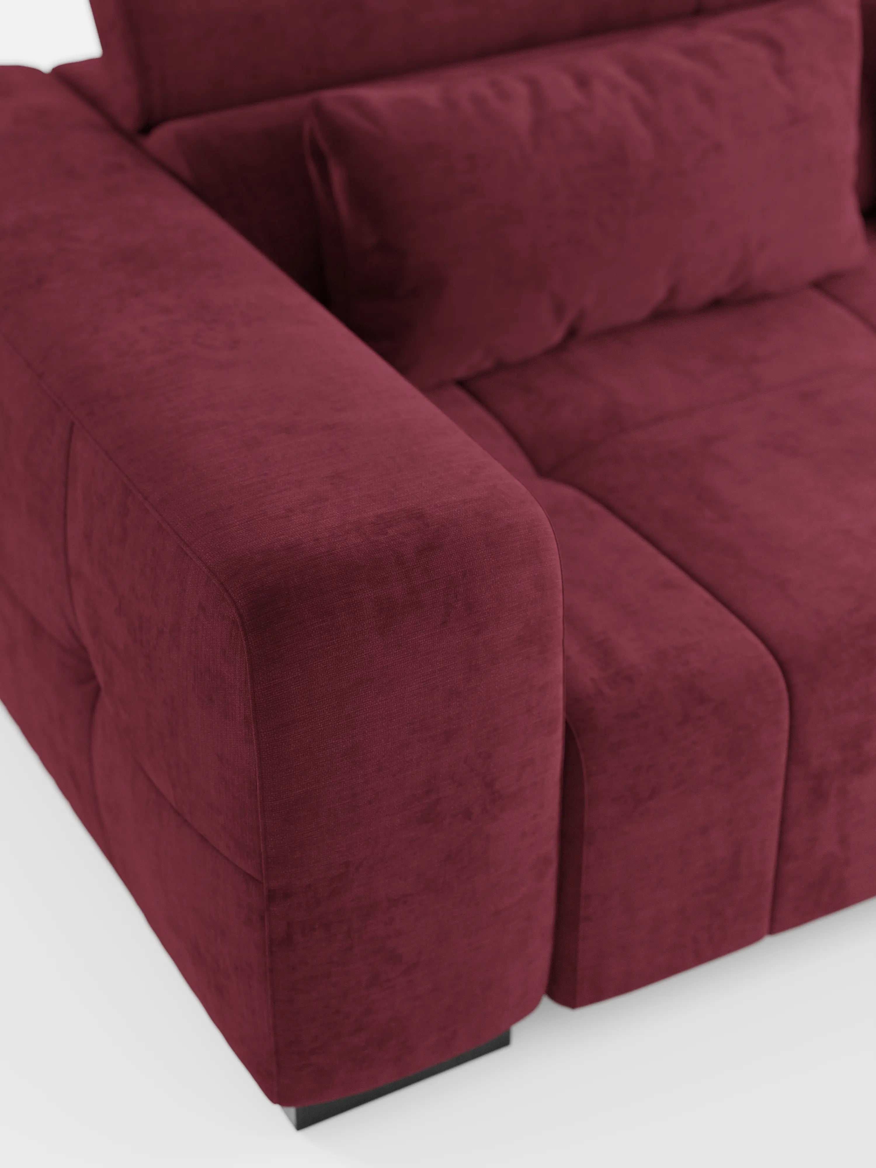 Primo piano del divano angolare Monarch con penisola e funzione Relax Elettrico per l'allungamento delle sedute di Divani.Store, rivestito in tessuto T31 smacchiabile color bordeaux scuro. L'ampio e morbido bracciolo presenta cuciture a vista e una consistenza soffice. Sono visibili parte dello schienale regolabile con poggiatesta reclinabili e il cuscino della seduta, il tutto su sfondo bianco.