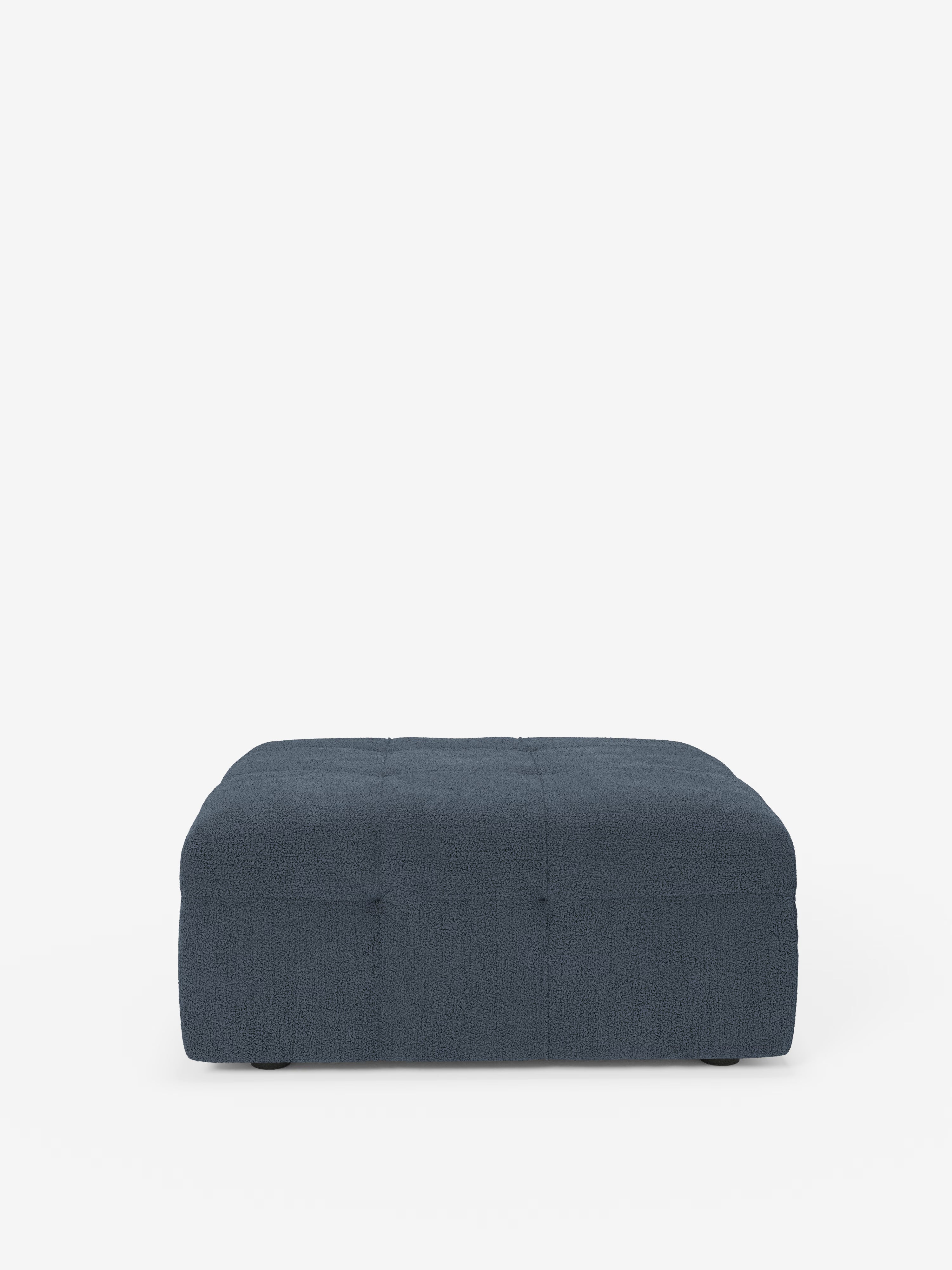 Un pouf basso e rettangolare della linea “Mosaic” di Divani.Store, realizzato in bouclé, con dimensioni di 96x77 cm e rivestito in tessuto T21 testurizzato e resistente alle macchie, spicca su uno sfondo bianco a tinta unita. Ispirato al classico design del pouf capitonné, questo pouf presenta delicati dettagli di trapuntatura quadrata sia sulla parte superiore che su quella frontale.