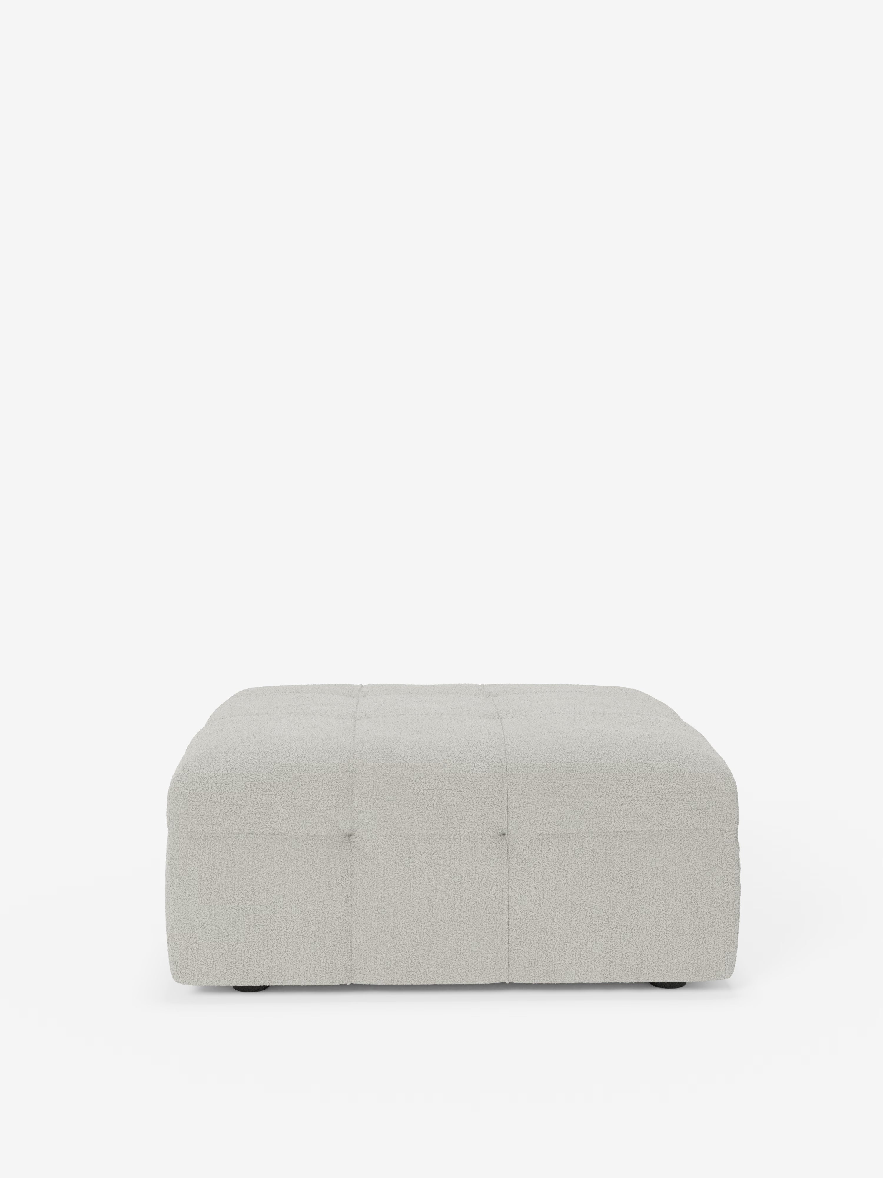 Un pouf quadrato in bouclé grigio chiaro, il modello “Mosaic pouf e modulo” di Divani.Store, presenta delicati dettagli capitonné sulla parte superiore e sui lati ed è rivestito in tessuto T21 antimacchia. Con il suo profilo basso e l’aspetto morbido e imbottito che richiama il design italiano, poggia su piedini piccoli e quasi invisibili su uno sfondo bianco a tinta unita.