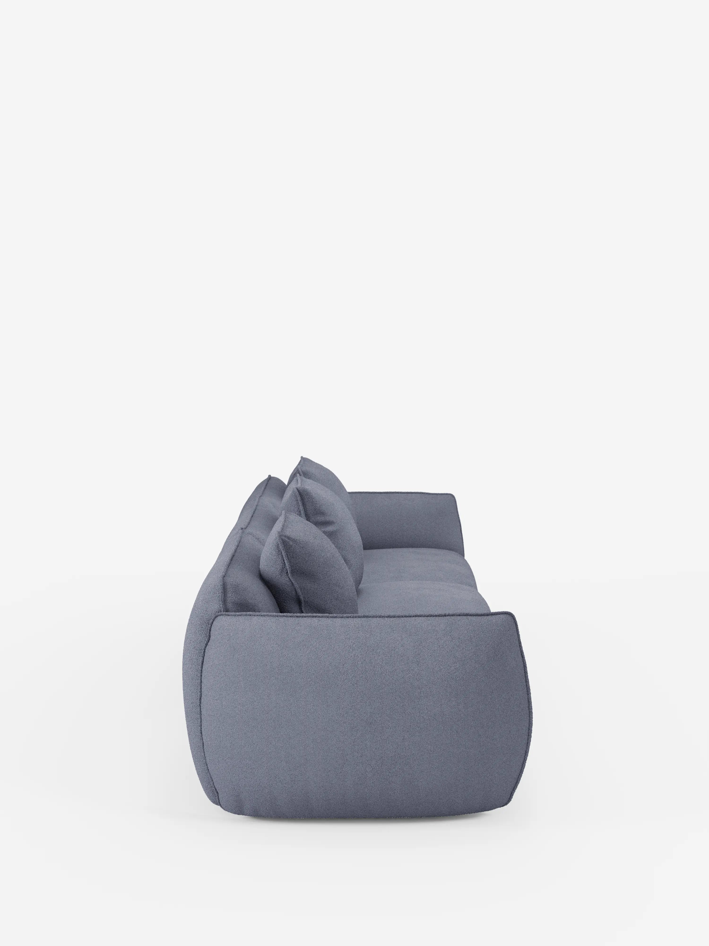 Vista laterale del divano modulare Nimbus a 3 posti, realizzabile in morbido tessuto smacchiabile effetto cotone T33 di Divani.Store, qui raffigurato in tessuto azzurro con una silhouette arrotondata e morbida. Sono visibili tre ampi cuscini di seduta e tre cuscini dello schienale abbinati, che ne sottolineano il design moderno. Questo elegante divano componibile per 5-6 persone è esposto su una superficie bianca su uno sfondo bianco a tinta unita.