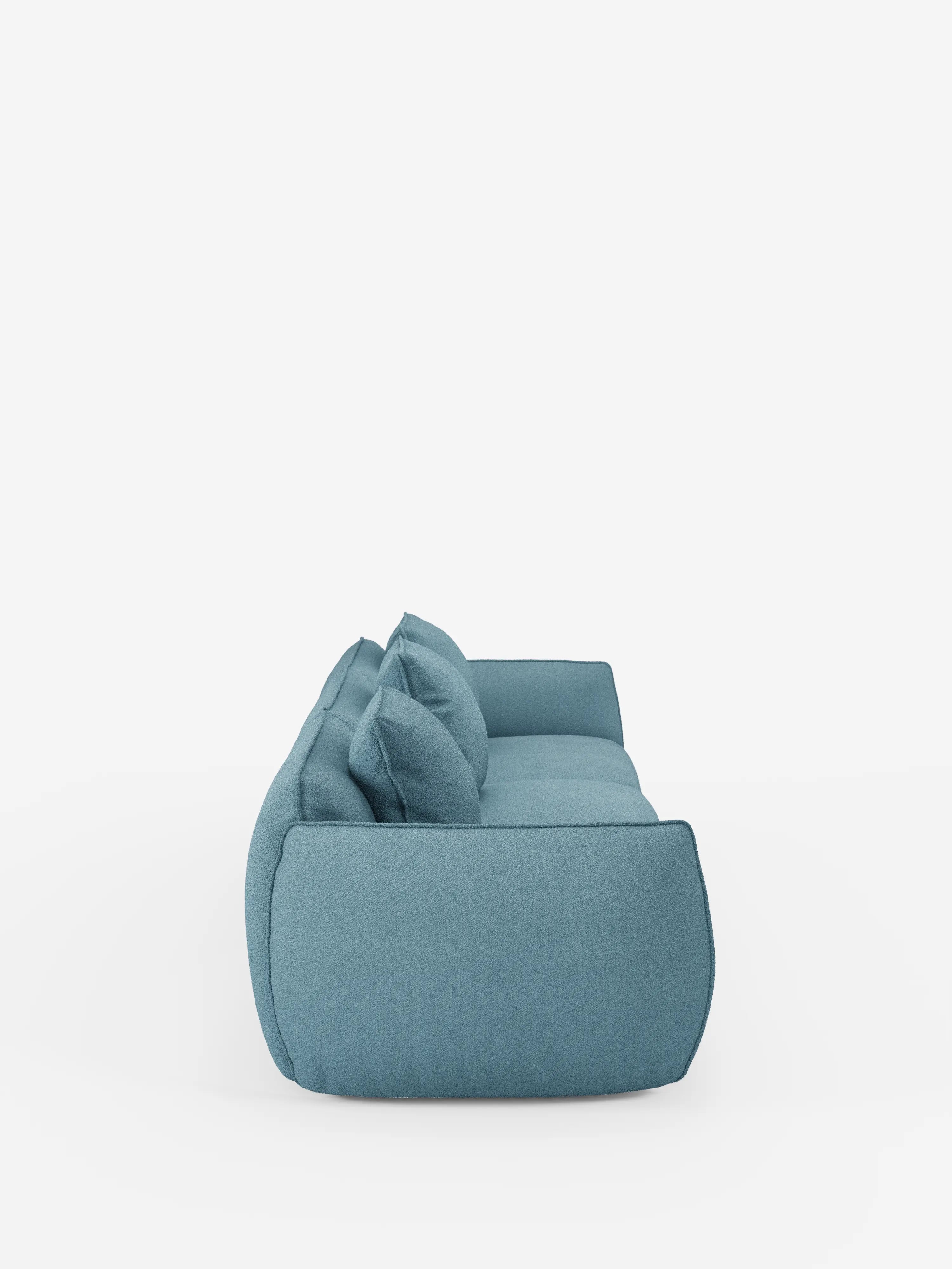 Vista laterale del divano modulare a 3 posti Nimbus, realizzabile in morbido tessuto smacchiabile effetto cotone T33 di Divani.Store, caratterizzato da un moderno rivestimento blu con due cuscini dello schienale e un unico cuscino di seduta. Questo lussuoso divano ha un aspetto morbido e accogliente, ampi braccioli ed è esposto su uno sfondo bianco a tinta unita, senza oggetti aggiuntivi.