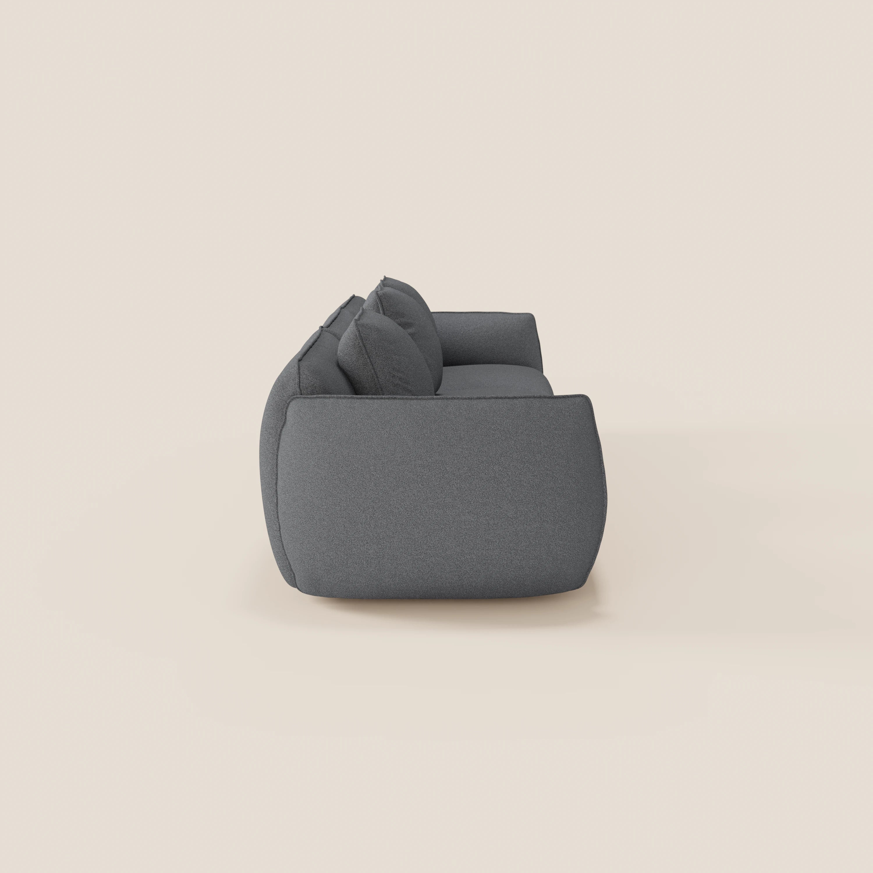 Una vista laterale del divano modulare a 3 sedute componibile Nimbus di Divani.Store in grigio scuro, con cuscini in tessuto felpato, bordi arrotondati e morbido tessuto smacchiabile effetto cotone T33, su uno sfondo beige chiaro.