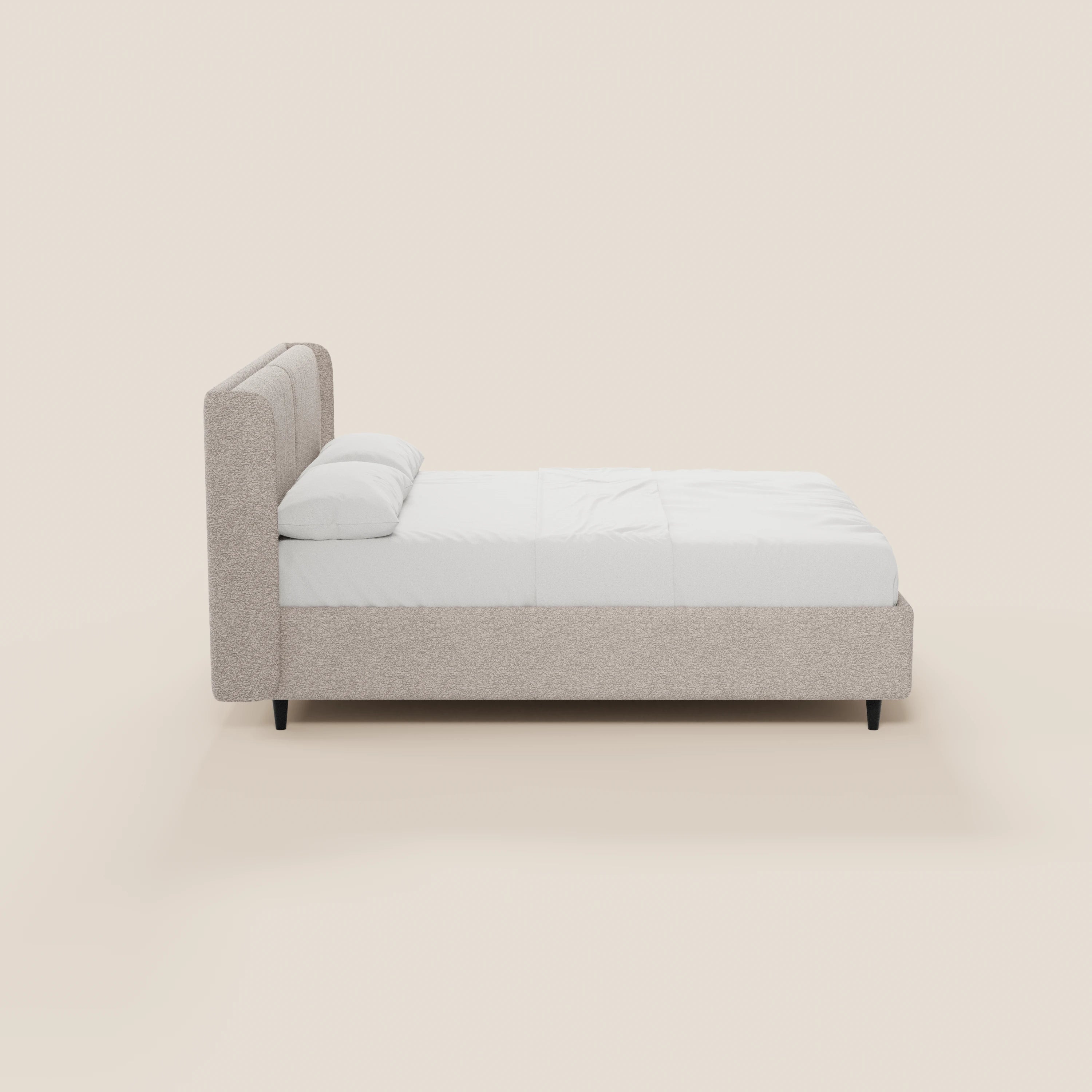 Una vista laterale del letto di design VALKIRIA di Letti.store, caratterizzato da una struttura rivestita in beige chiaro certificato Oeko-Tex® con testiera avvolgente, due cuscini imbottiti, biancheria da letto bianca e gambe corte scure su uno sfondo chiaro e semplice.