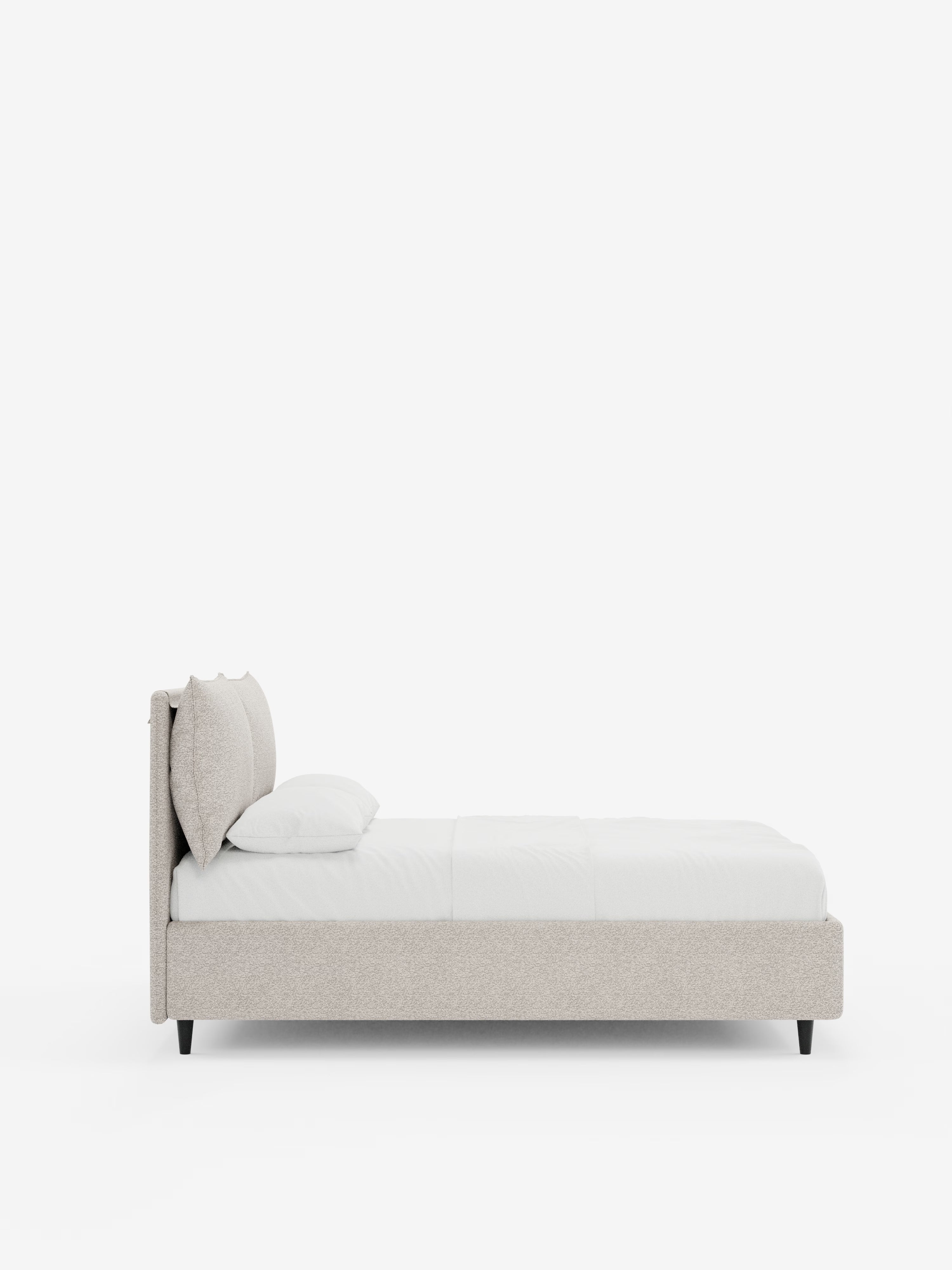 Un moderno letto imbottito ZAYRON di Letti.store, caratterizzato da una struttura in tessuto beige chiaro certificato Oeko-Tex®, gambe basse nere e biancheria da letto di un bianco brillante. Due cuscini poggiano contro l’alta testata regolabile, dalle linee morbidamente curve, dotata di cuscini regolabili. Sullo sfondo bianco a tinta unita, il design minimalista e lo spazio contenitivo integrato del letto risaltano con eleganza.